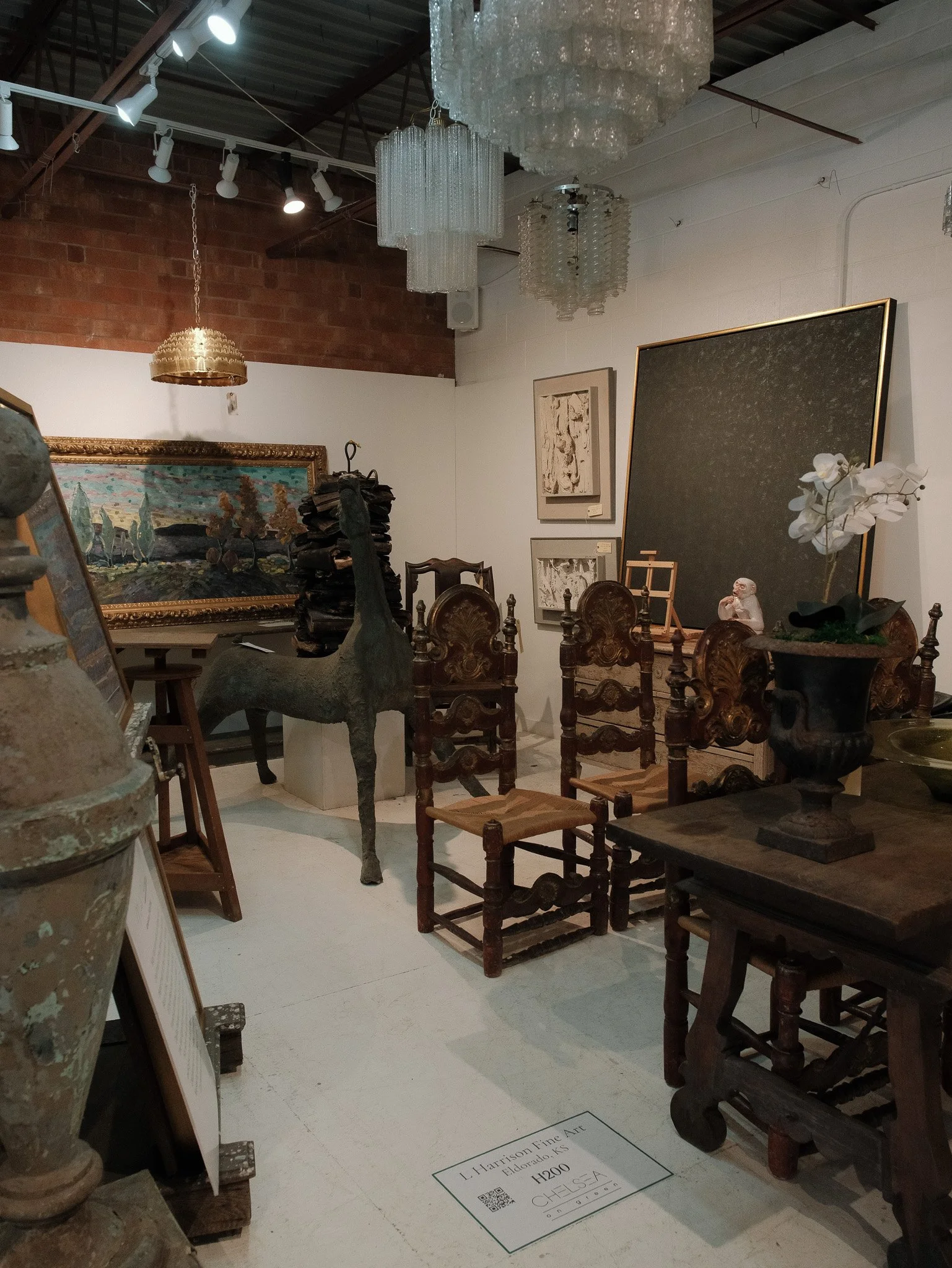 Interior of an art gallery with paintings, sculptures, and vintage wooden chairs on display.