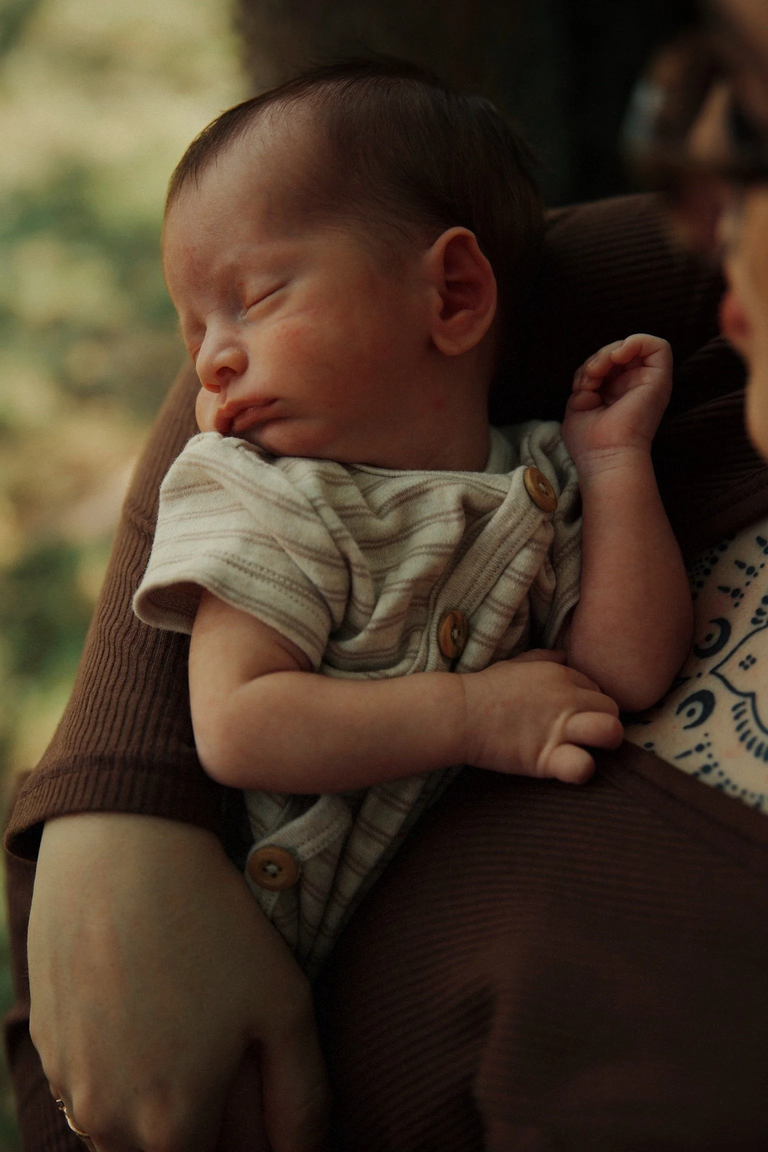 A close-up of a sleeping young child resting on an adult's shoulder, with a warm indoor background.