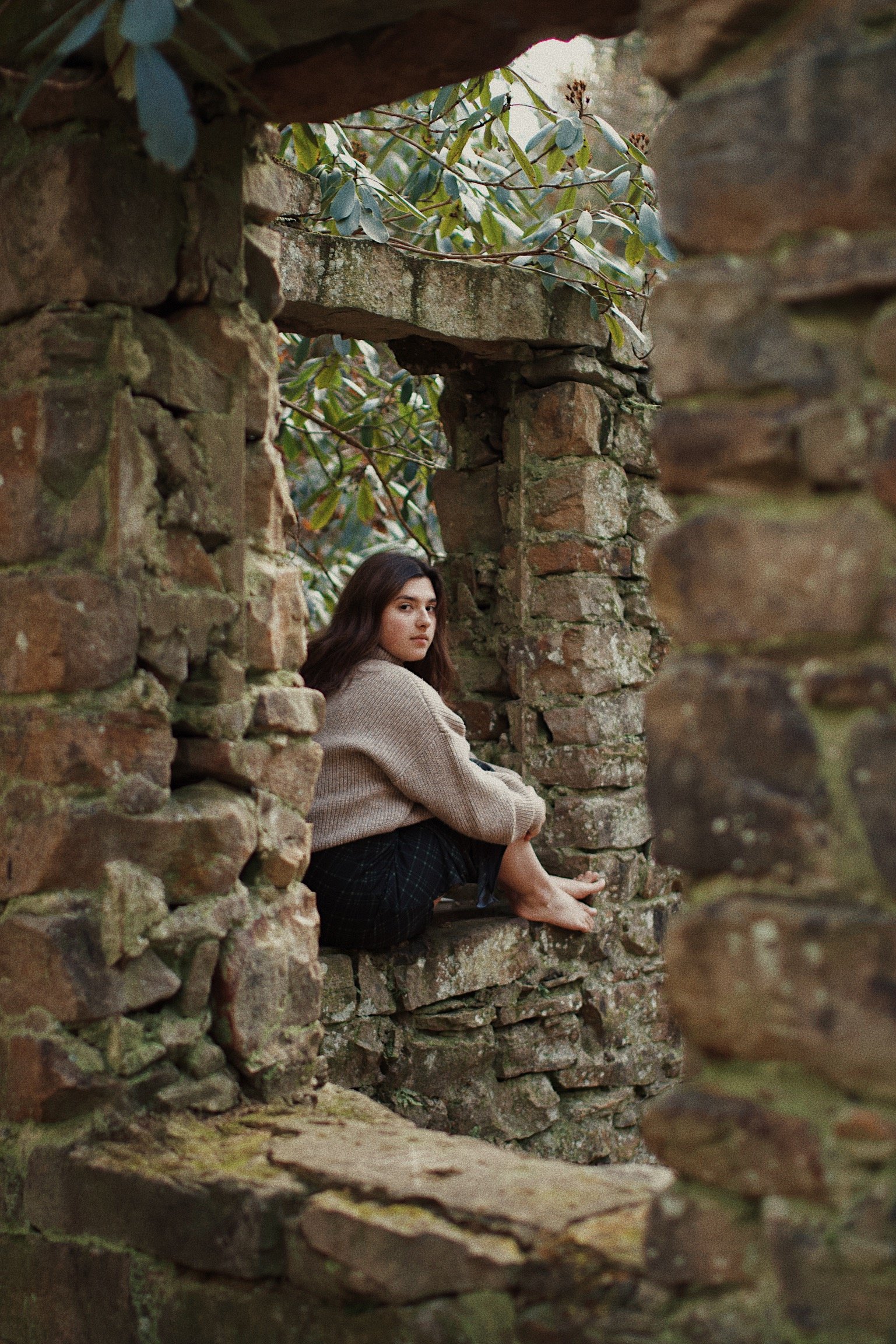 A young woman sitting on a stone ledge surrounded by old brick ruins with greenery.
