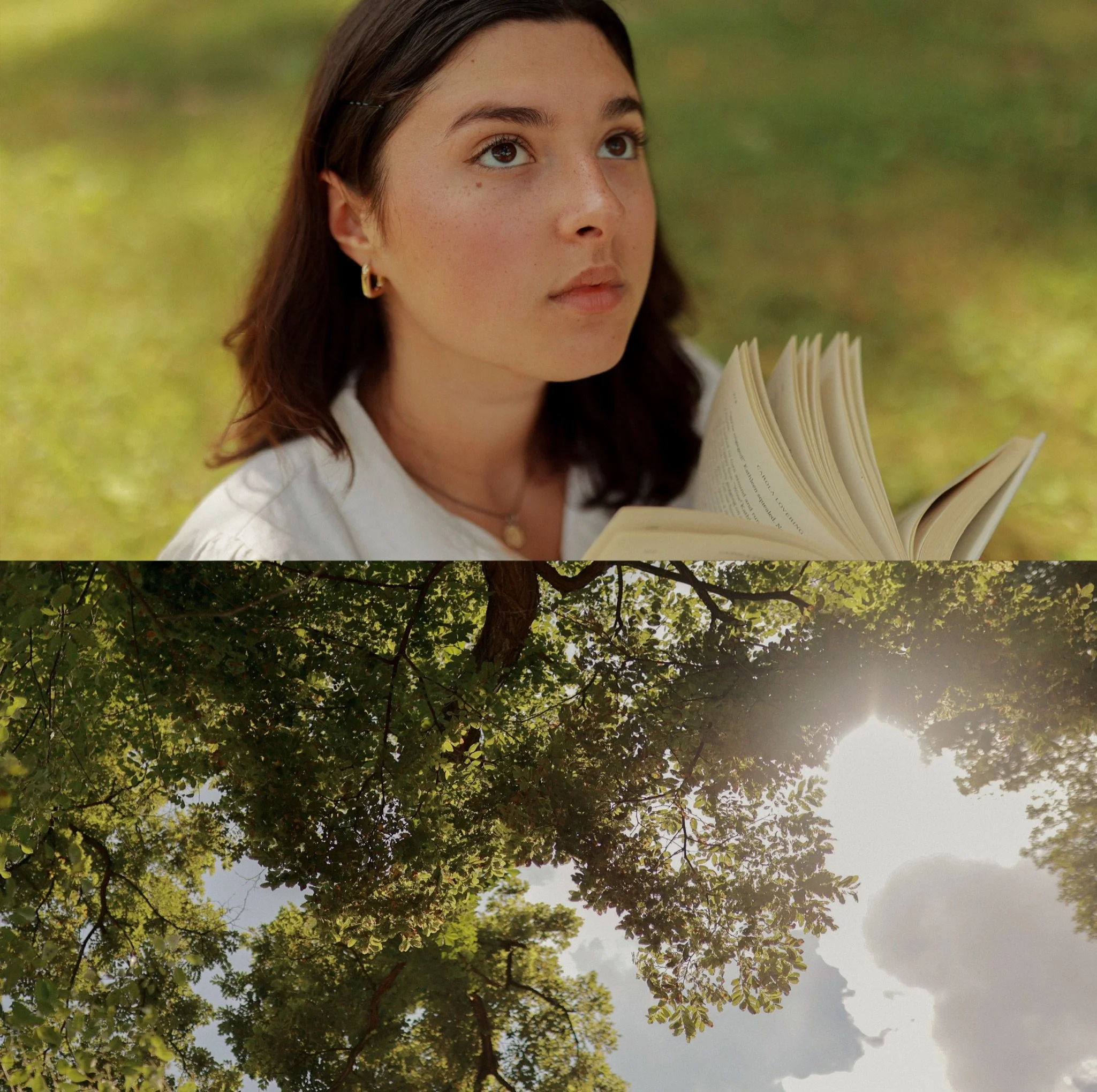 A young woman with brown hair and earrings holds an open book outdoors, with a background of green foliage and trees.