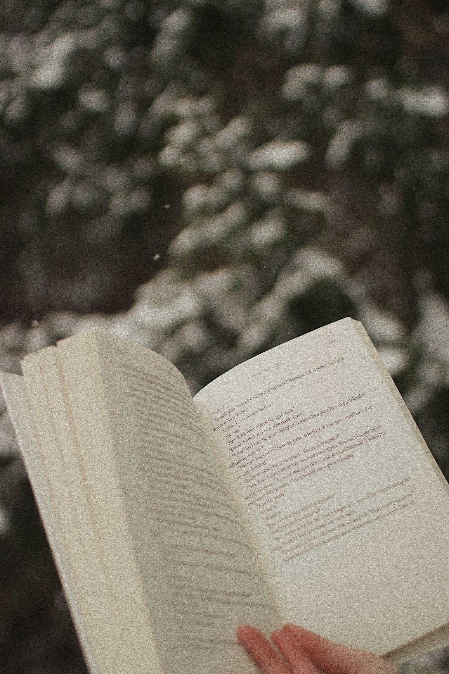 A person holding an open book outdoors with snow-covered trees in the background.