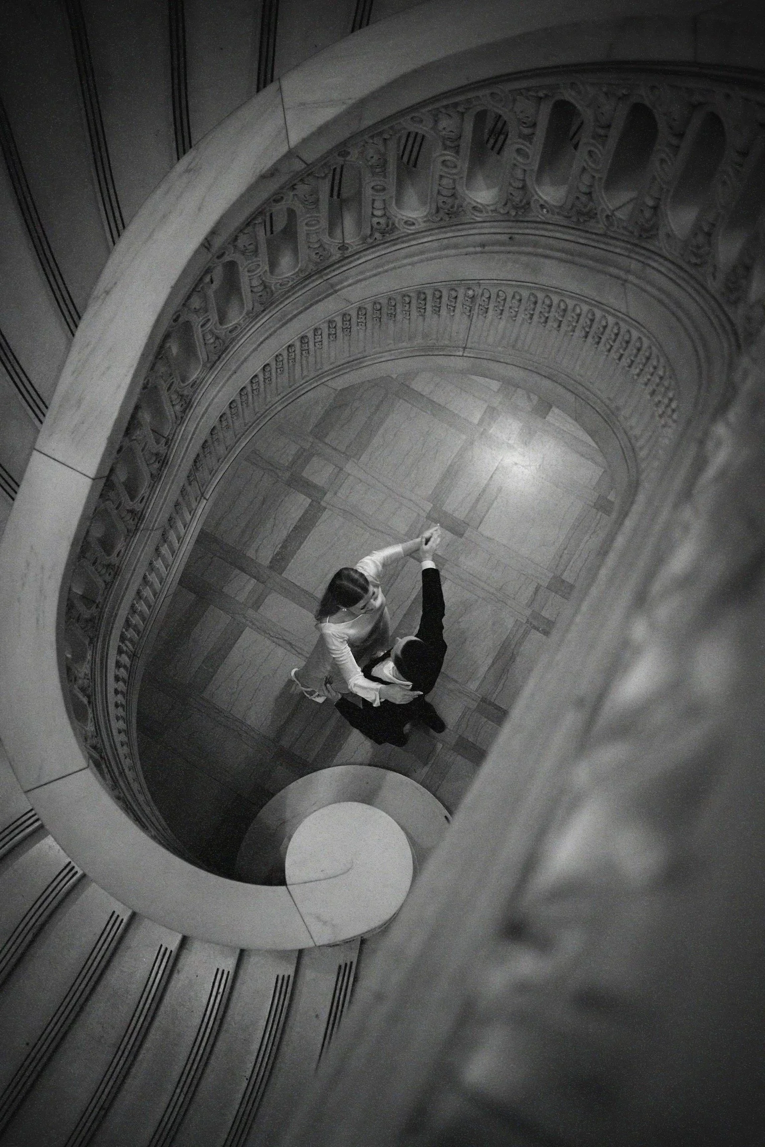A view looking down a spiral staircase with two people dancing on the floor below.