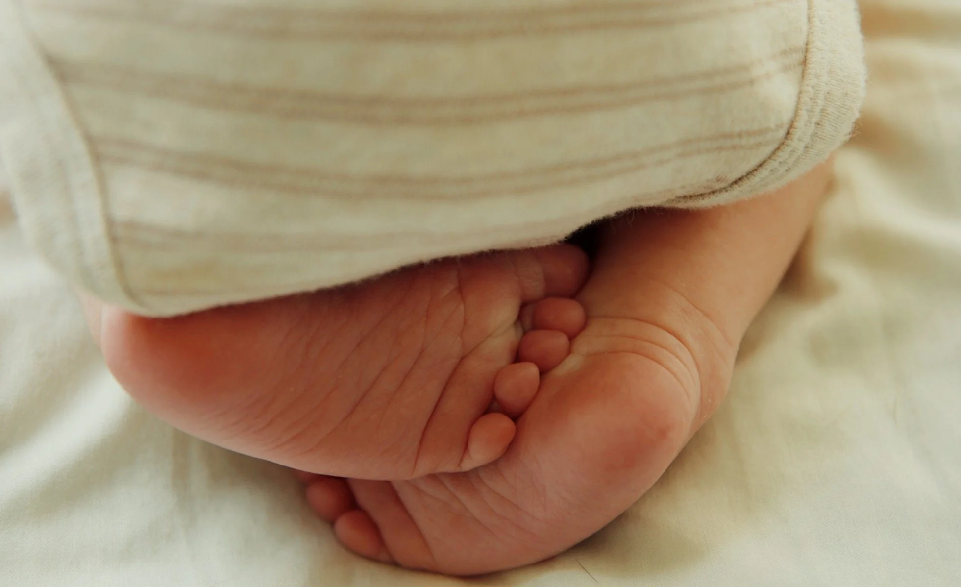 Close-up of a newborn baby's tiny hand curled into a fist, resting on a soft surface, partly covered by a beige striped cloth.