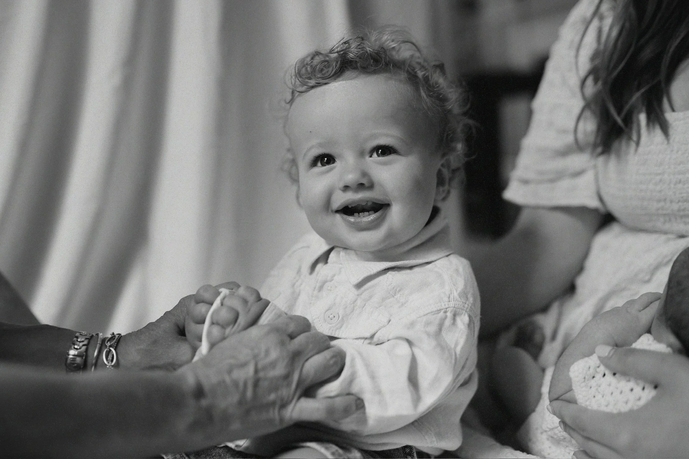 A young child with curly hair smiling while holding hands with an elderly person.