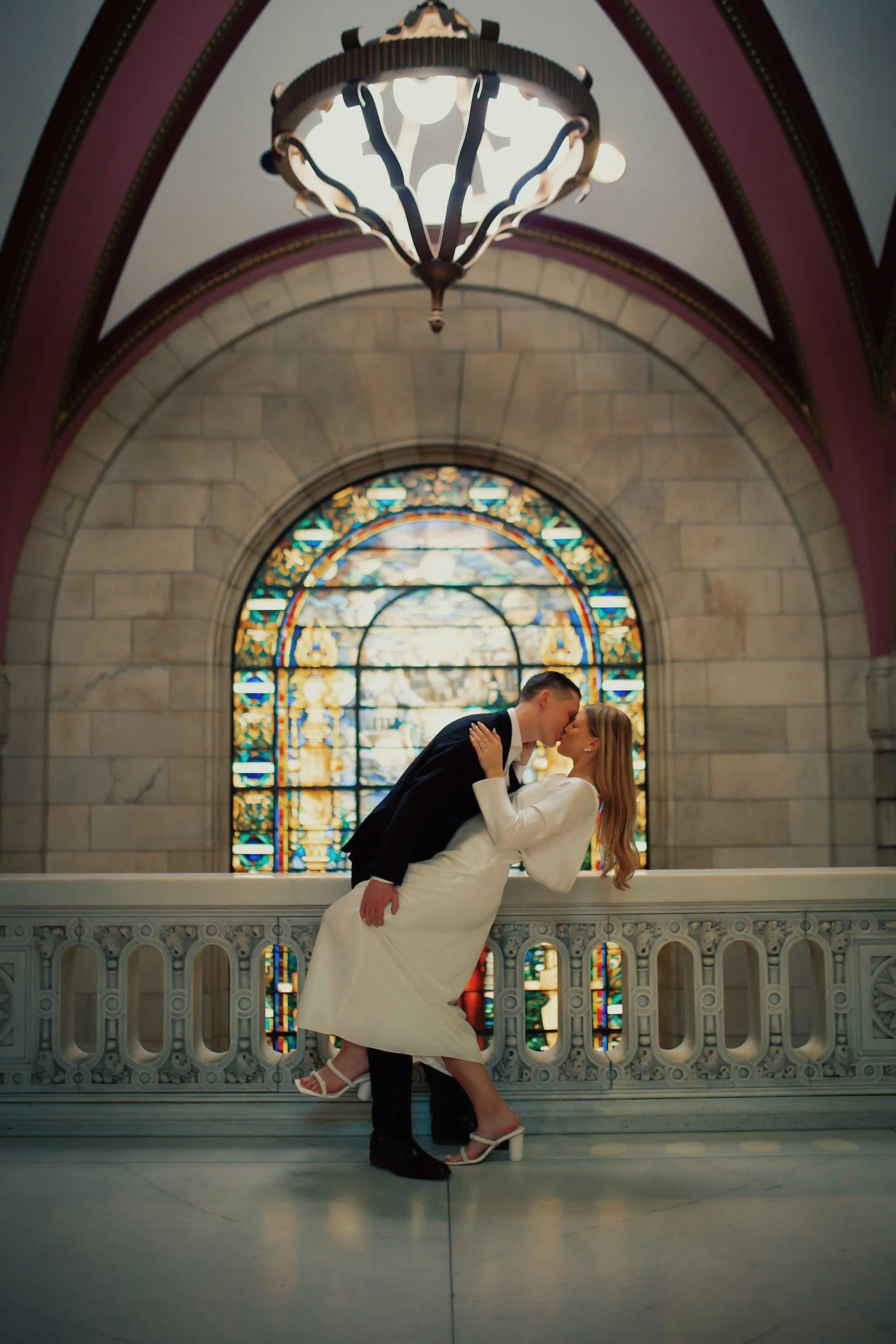 A newlywed couple sharing a kiss inside a church with a stained glass window in the background.