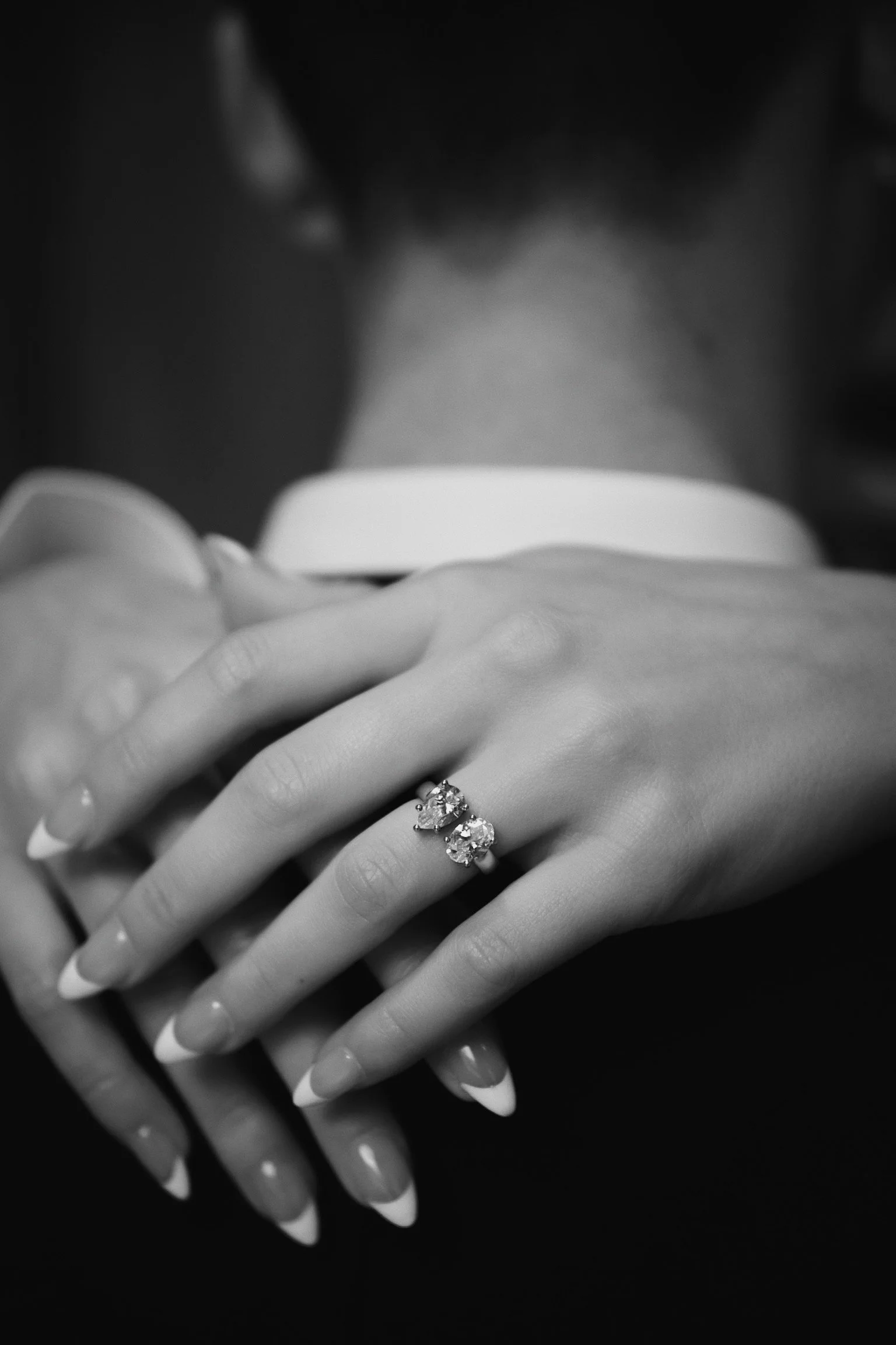 Close-up of a woman's hand with two rings featuring large gemstones, resting on her lap, in black and white.