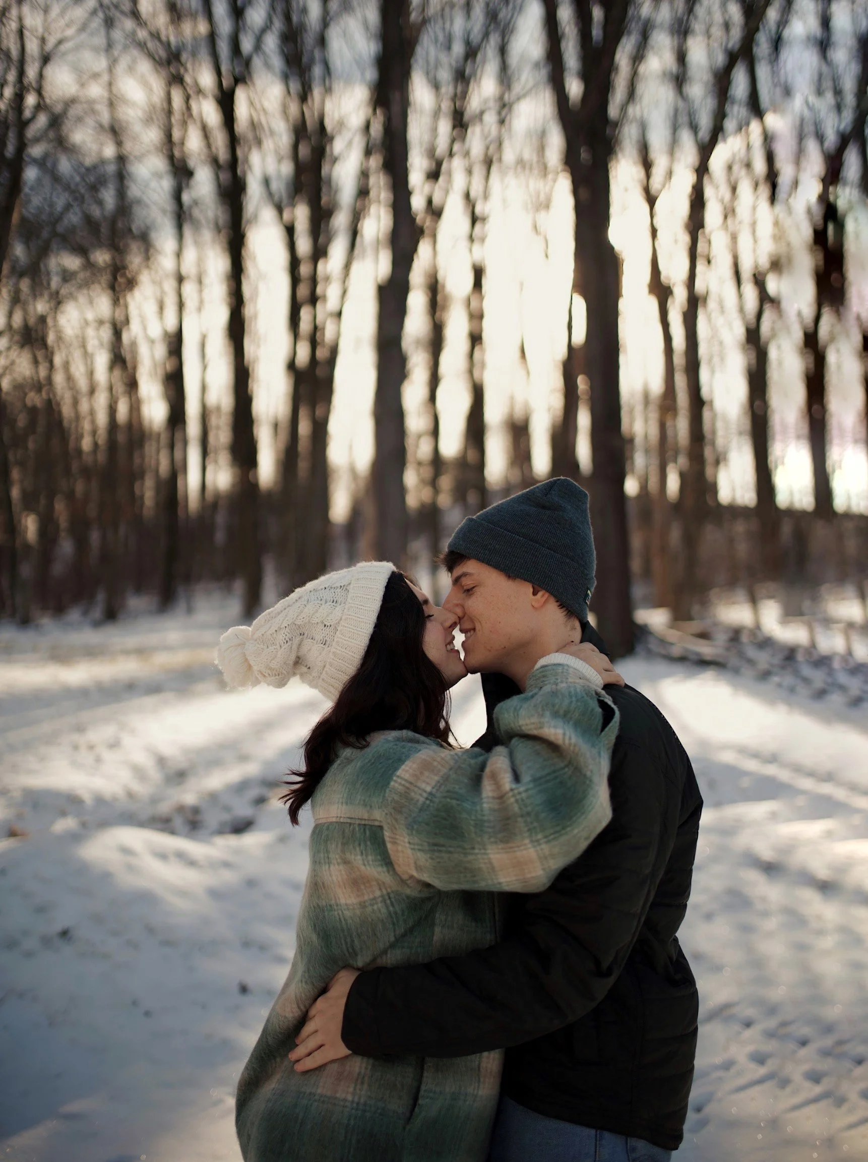Couple hugging and smiling in a snowy forest during winter.