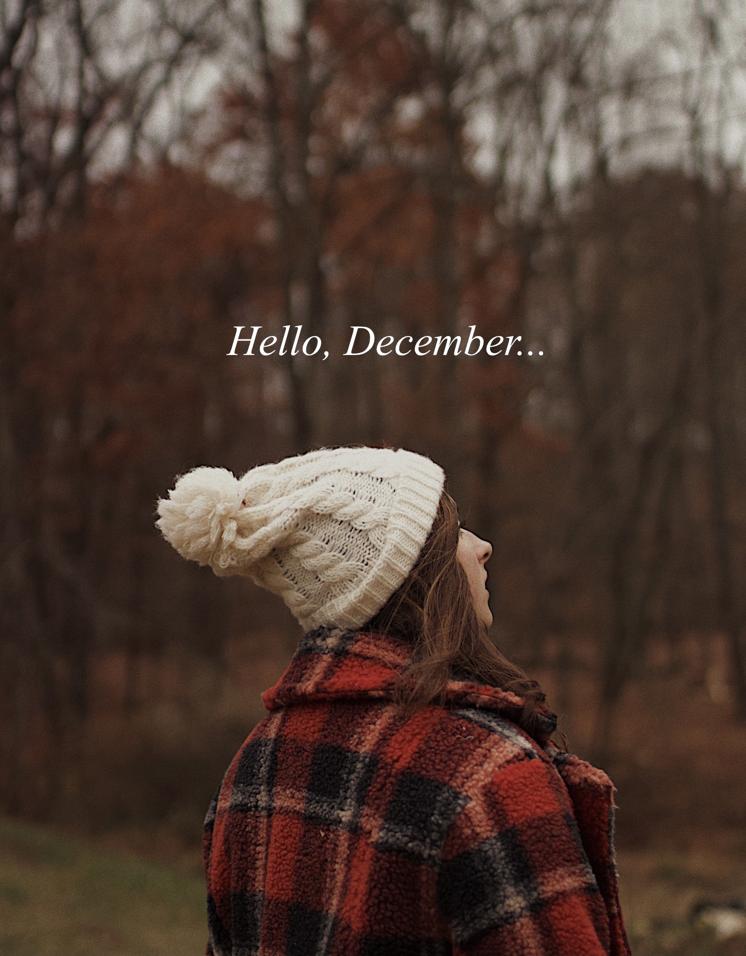 A woman in a red and black plaid jacket and a white knit beanie standing outdoors in front of a background of trees with brown leaves. The text on the image reads, 'Hello, December...'.