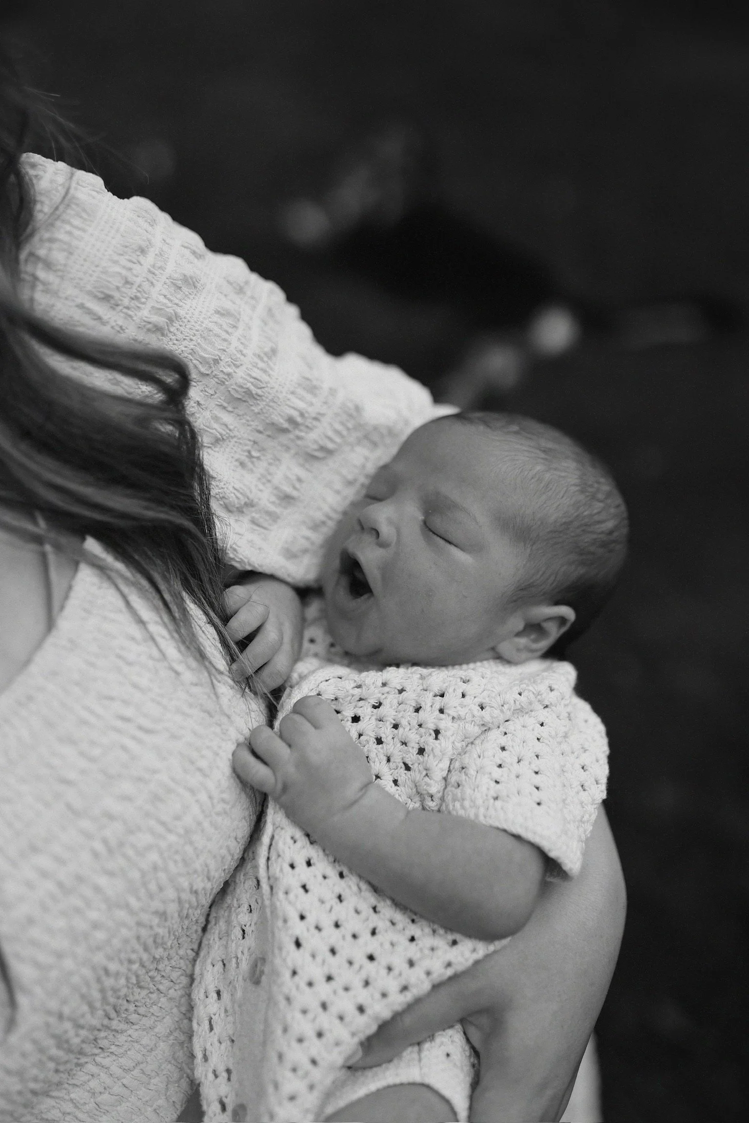 A person holding a yawning newborn baby wrapped in a crocheted blanket.