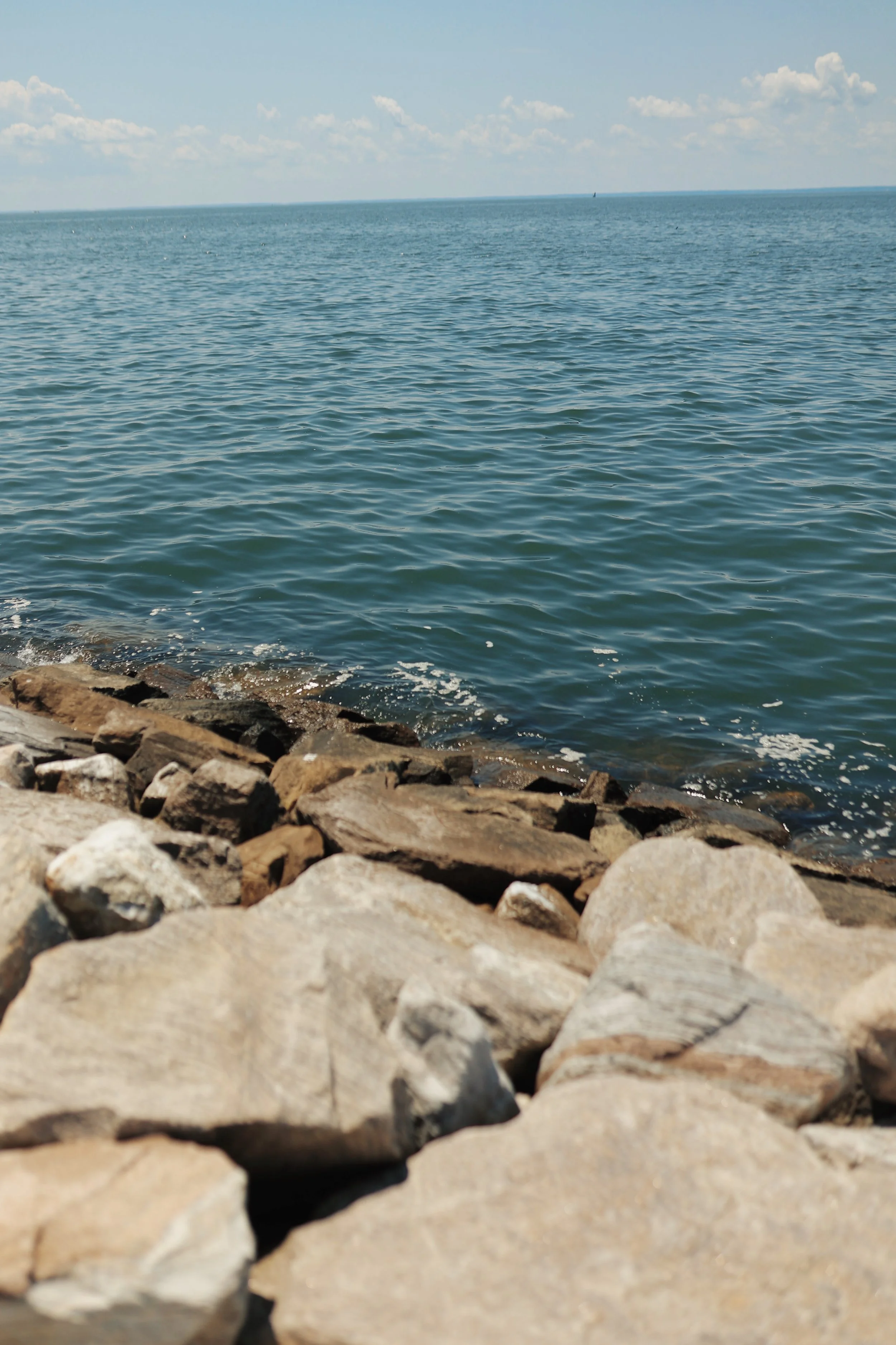 View of a rocky shoreline with calm ocean water and a partly cloudy sky in the background.