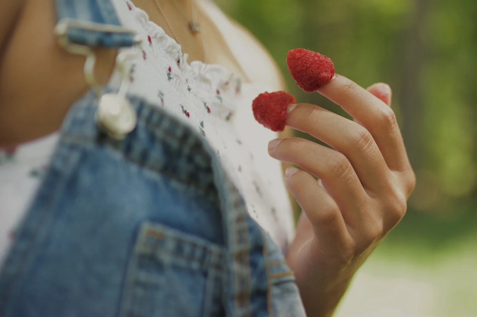 Person holding two raspberries on their fingers, with part of their clothing and background visible.
