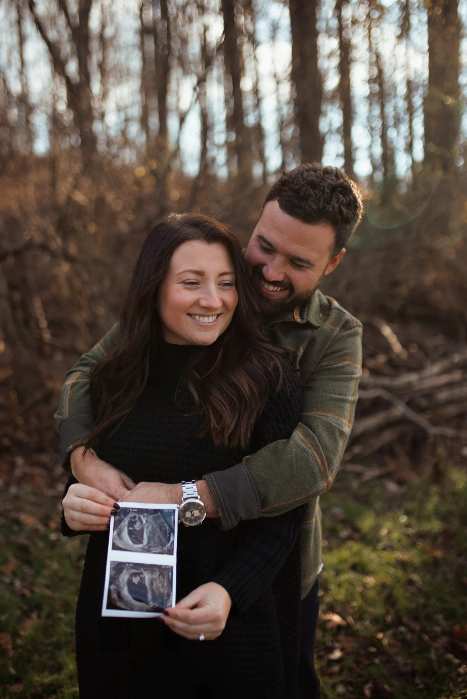A happy couple celebrating pregnancy with an ultrasound in a wooded outdoor setting.