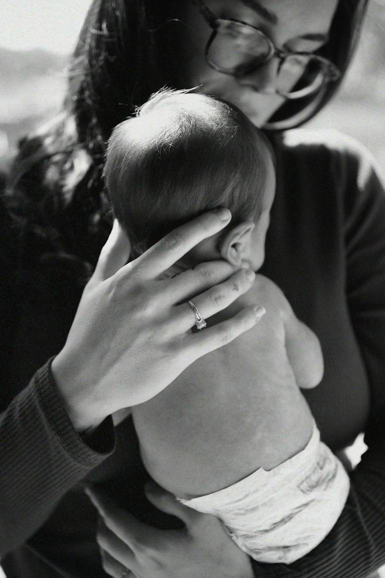 A woman holding a sleeping baby close to her chest, with her hand gently resting on the baby's head, in a black and white photo.