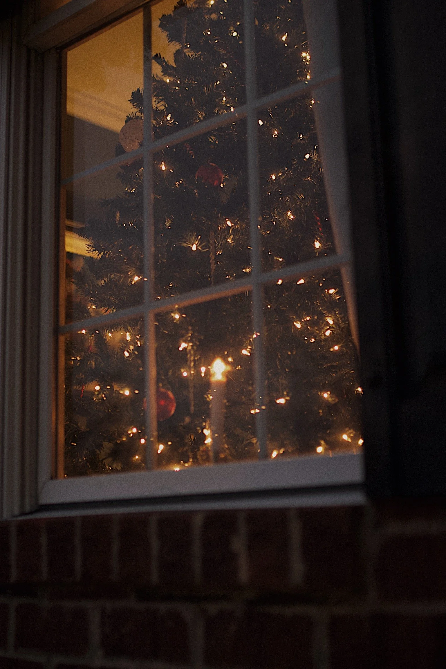 A decorated Christmas tree with lights and ornaments seen through a window at night.