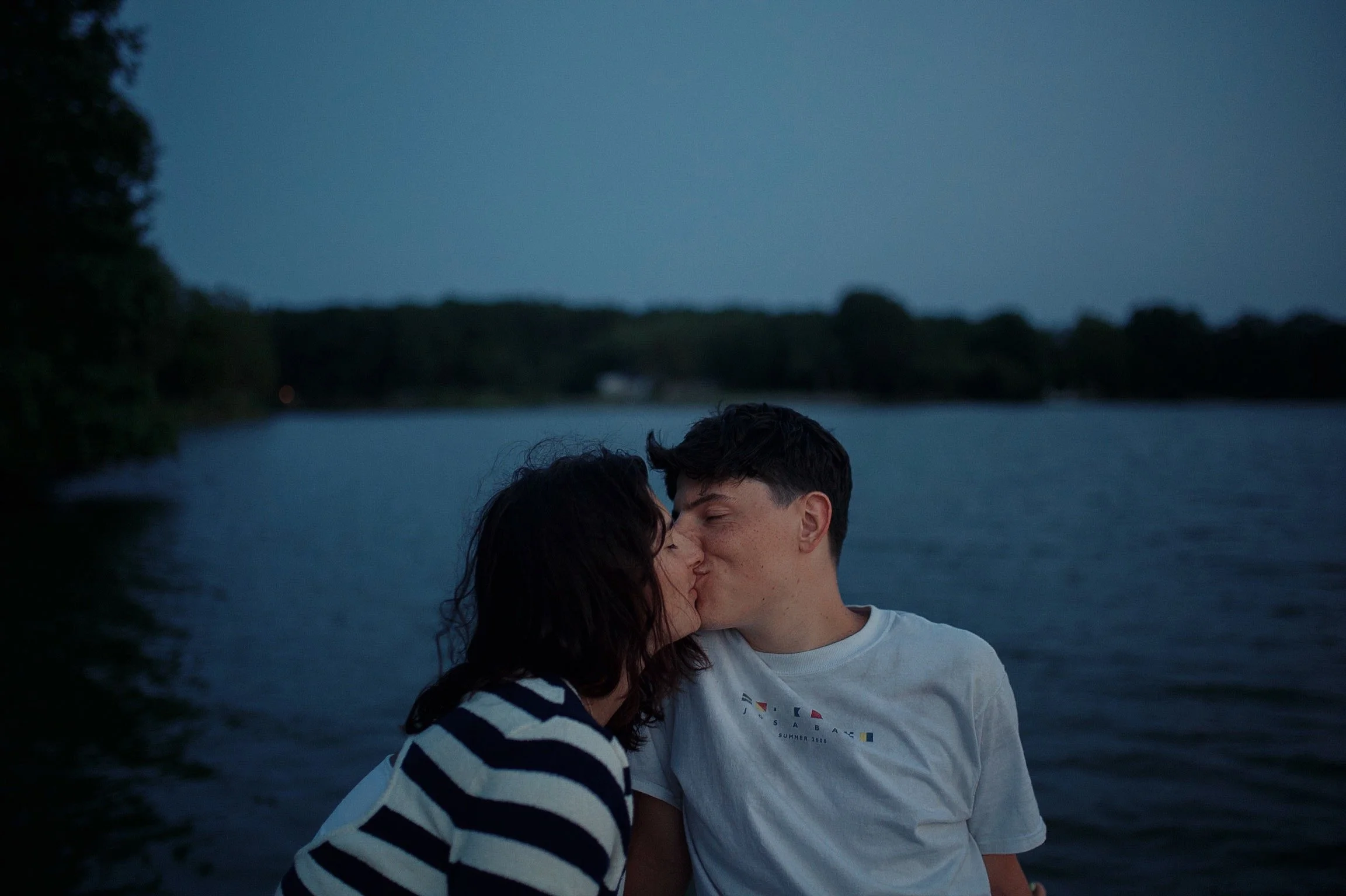 A young couple sharing a kiss near a body of water during twilight.