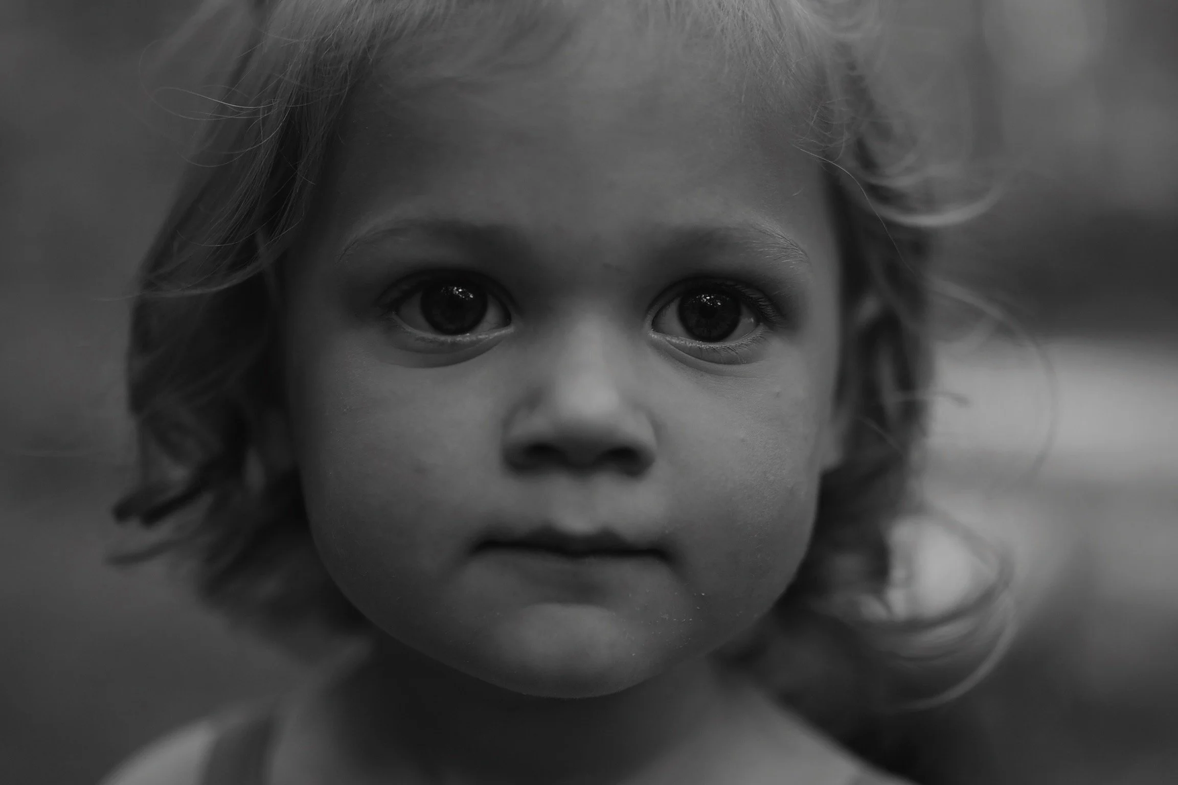 Close-up black and white portrait of a young child with curly hair and large, expressive eyes.