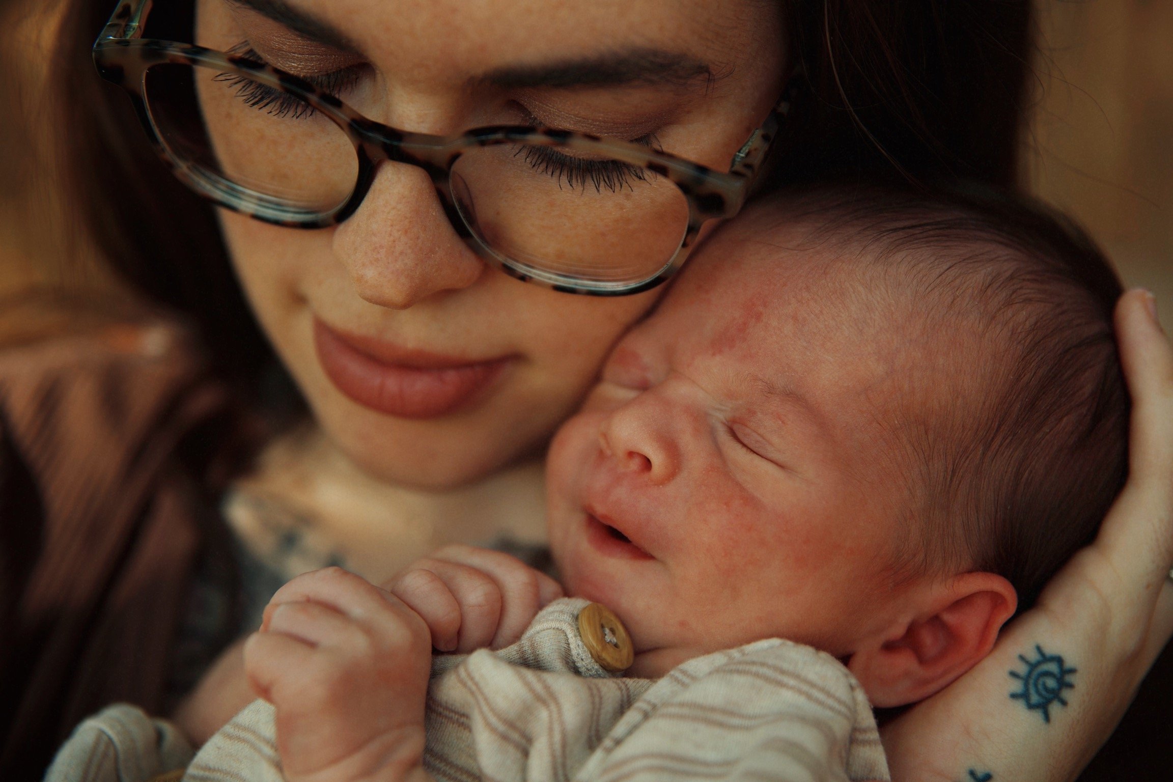 A woman with glasses holding a sleeping infant close to her face, both with peaceful expressions.