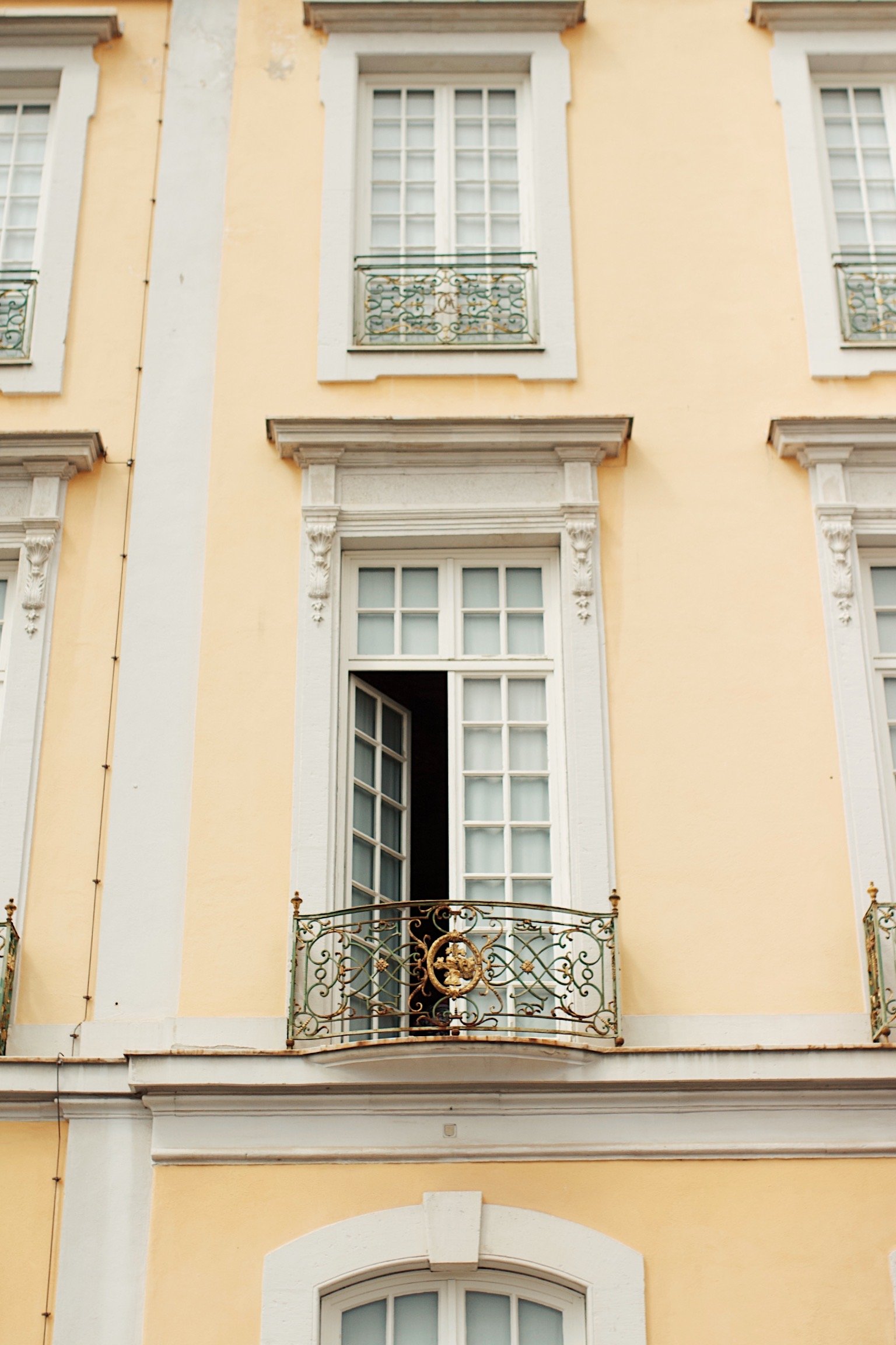 Close-up of a yellow building with white trim, featuring tall windows and ornate metal balconies with gold accents.