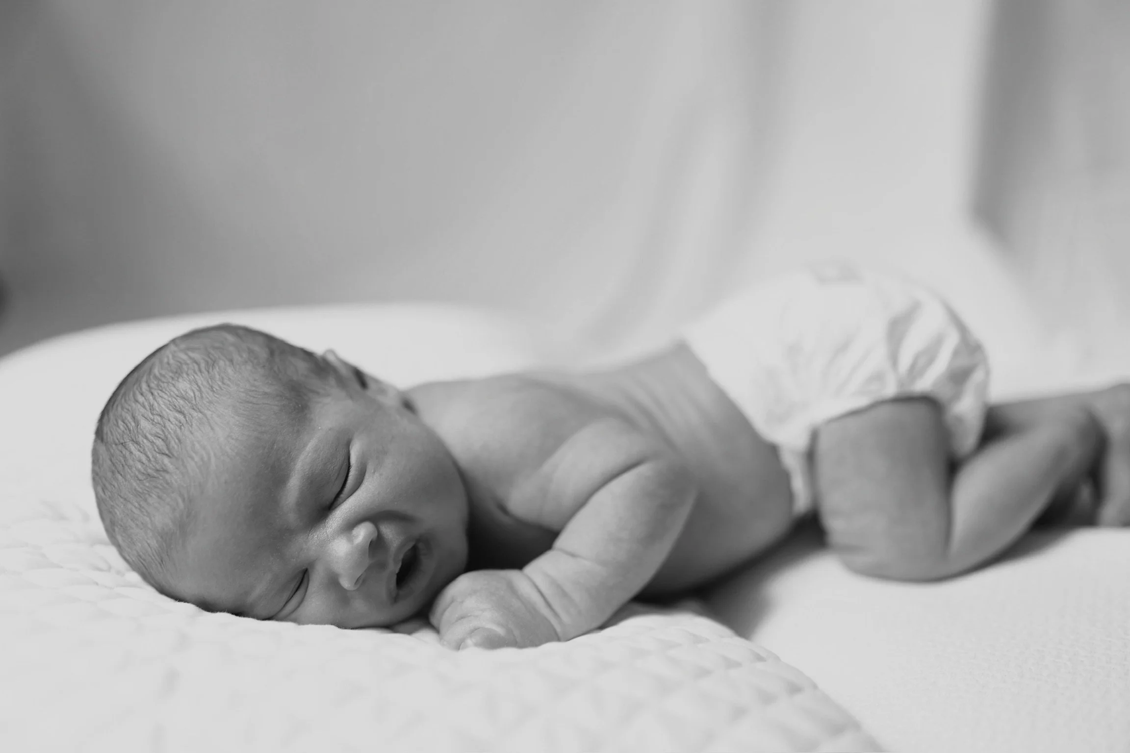 Black and white photo of a newborn baby sleeping on a soft surface, wearing a diaper.