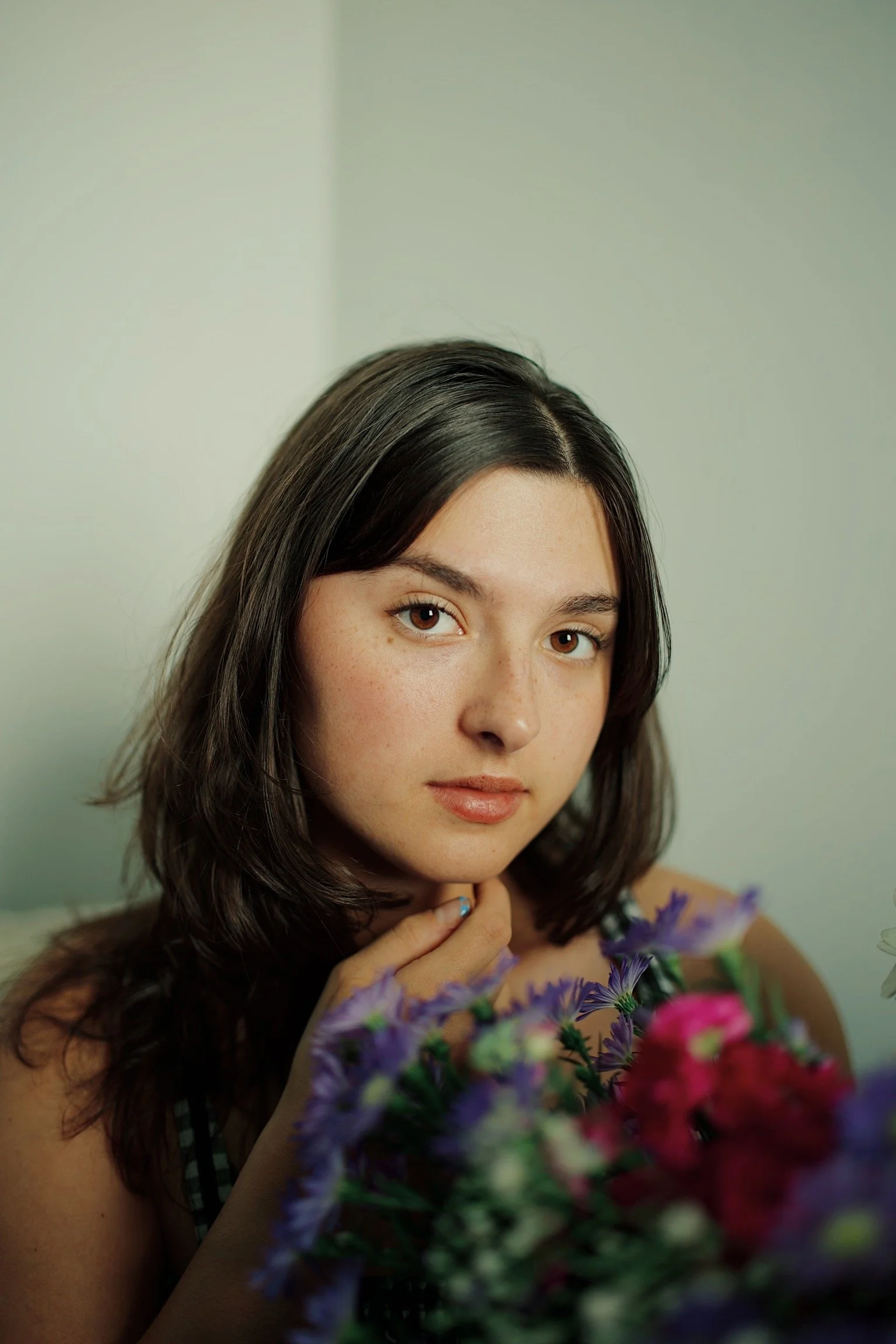 A young woman with shoulder-length dark hair, light skin, and freckles, gazing at the camera while holding a colorful bouquet of flowers.