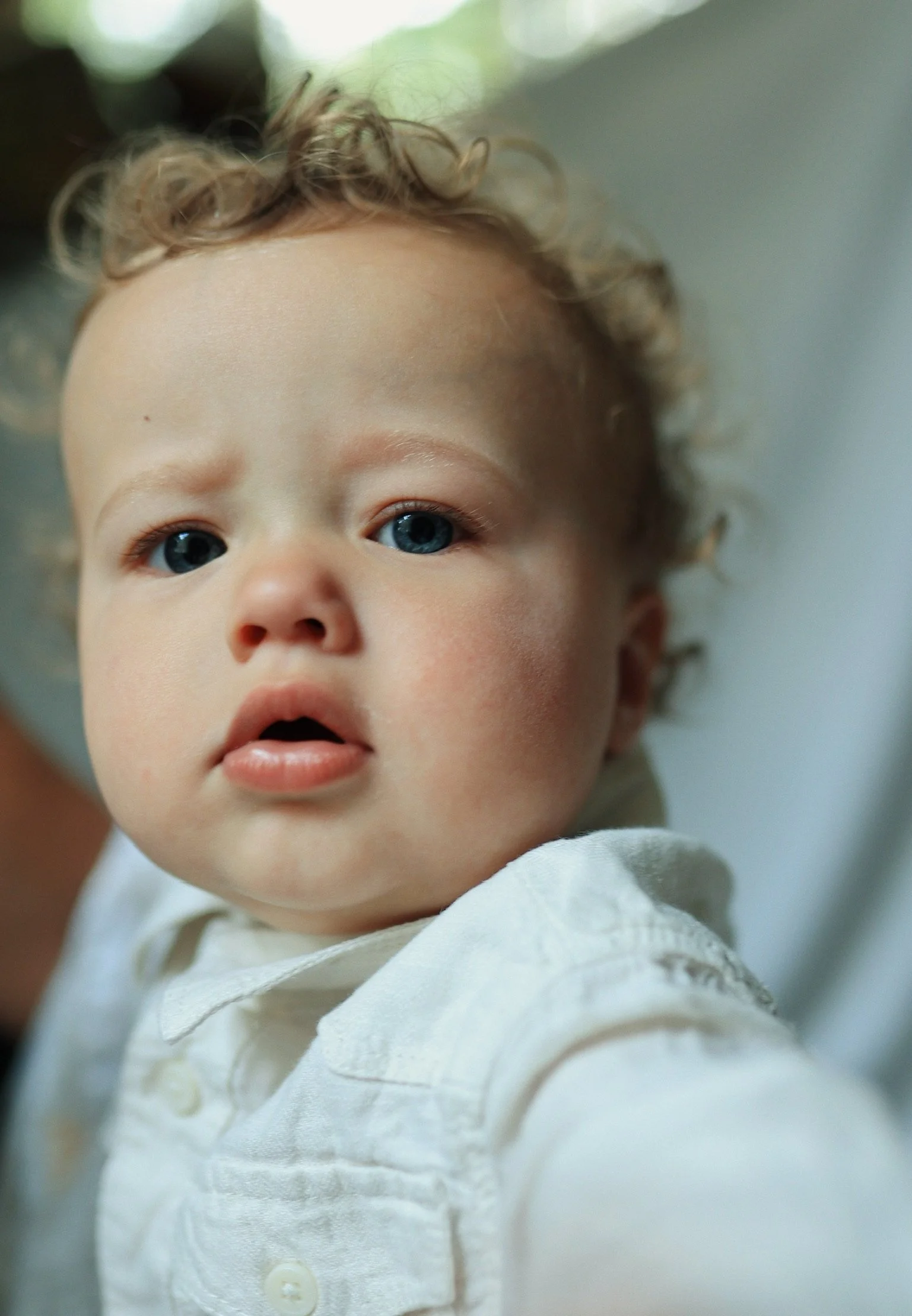 Close-up of a young child with blue eyes and curly blonde hair, wearing a white shirt.
