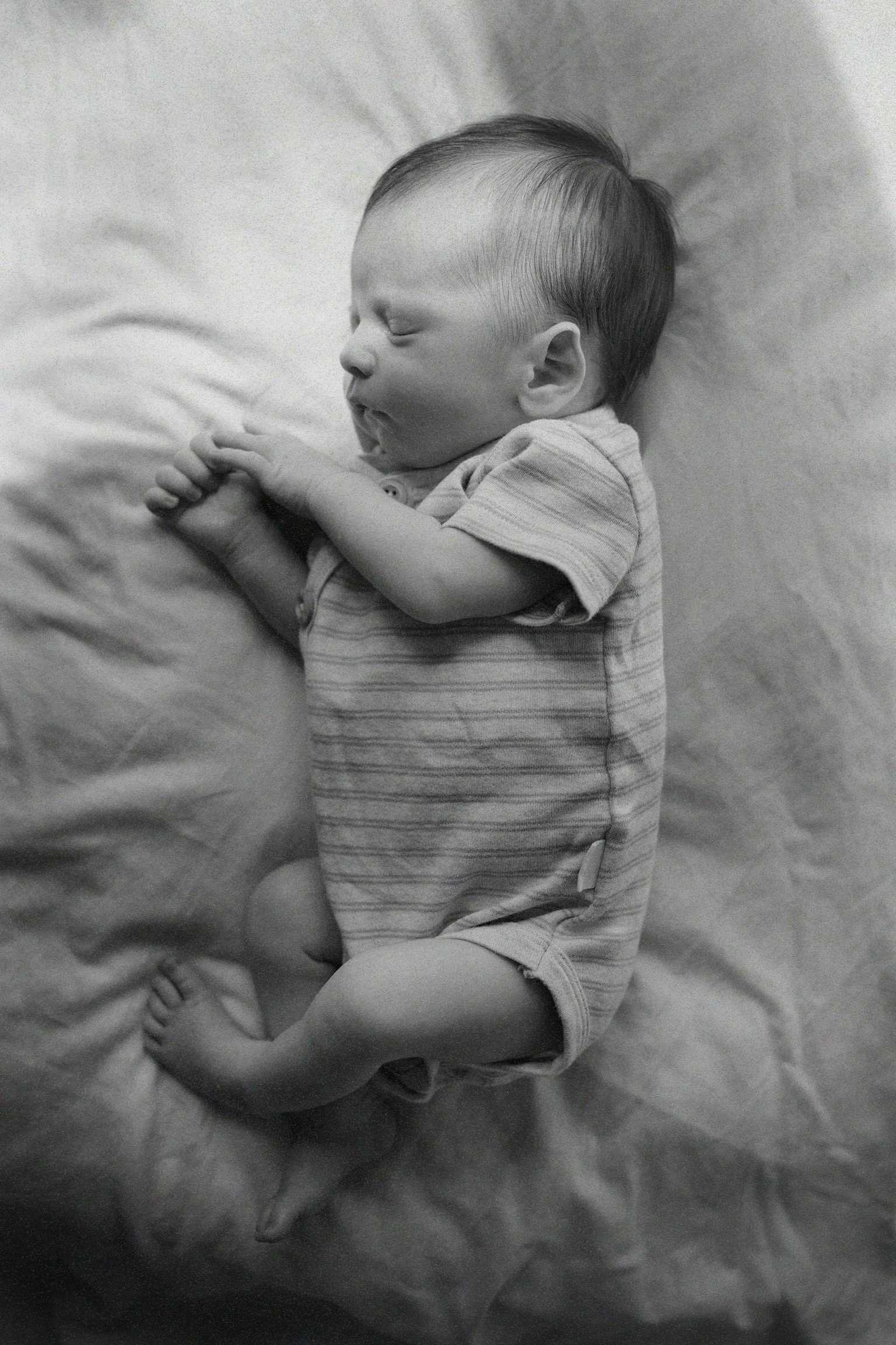 A sleeping baby lying on a soft blanket, with arms crossed and eyes closed.