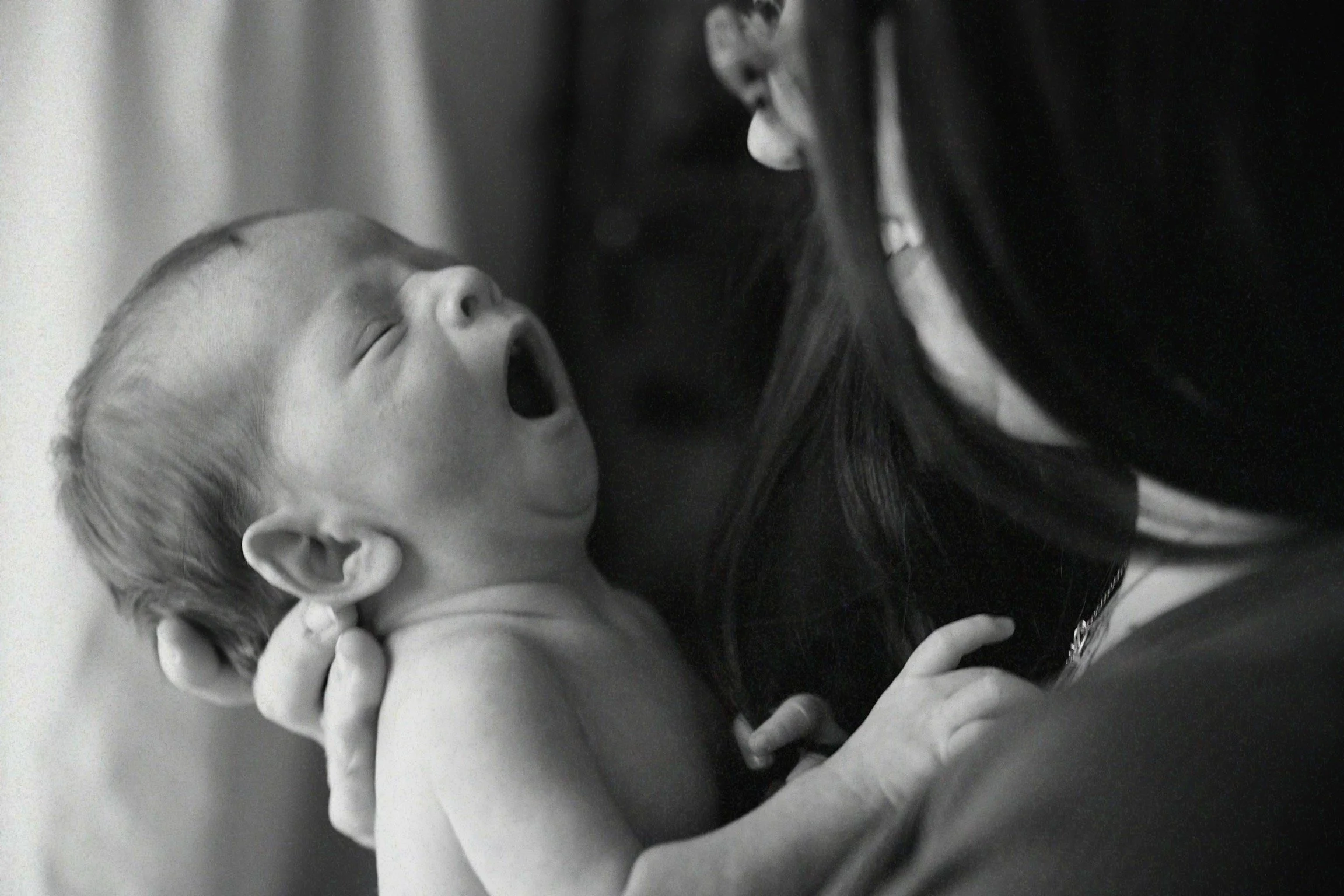 A woman holding a yawning baby close to her face, in black and white.