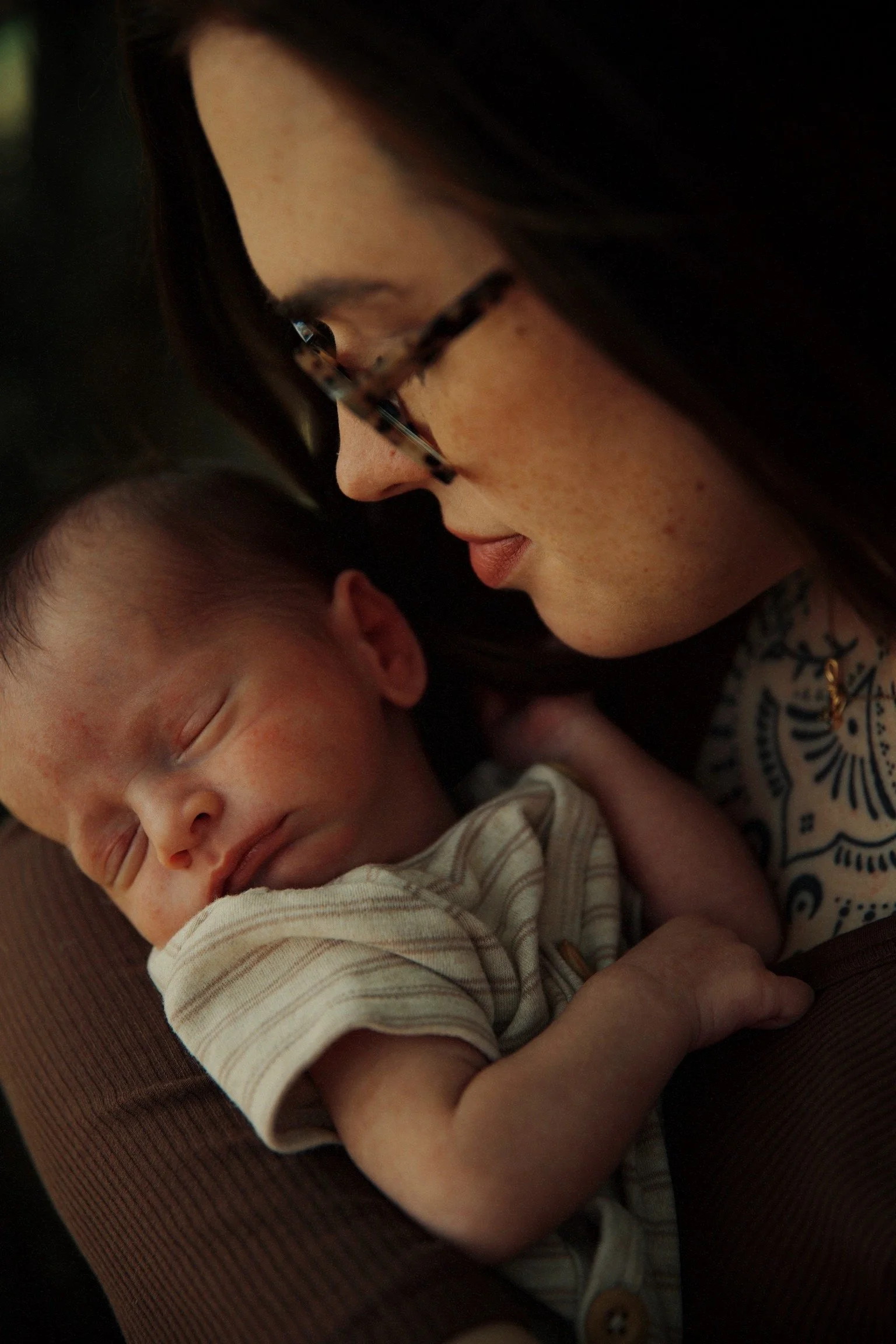 A woman holding a sleeping newborn baby close to her face with her forehead near the baby's head.