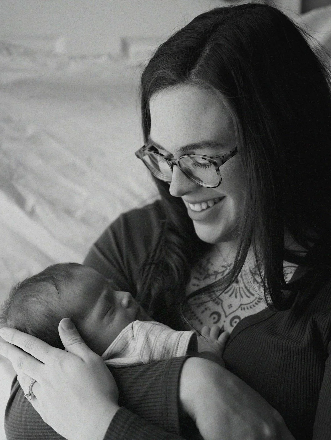 A woman wearing glasses holds a newborn baby, smiling lovingly at the baby.