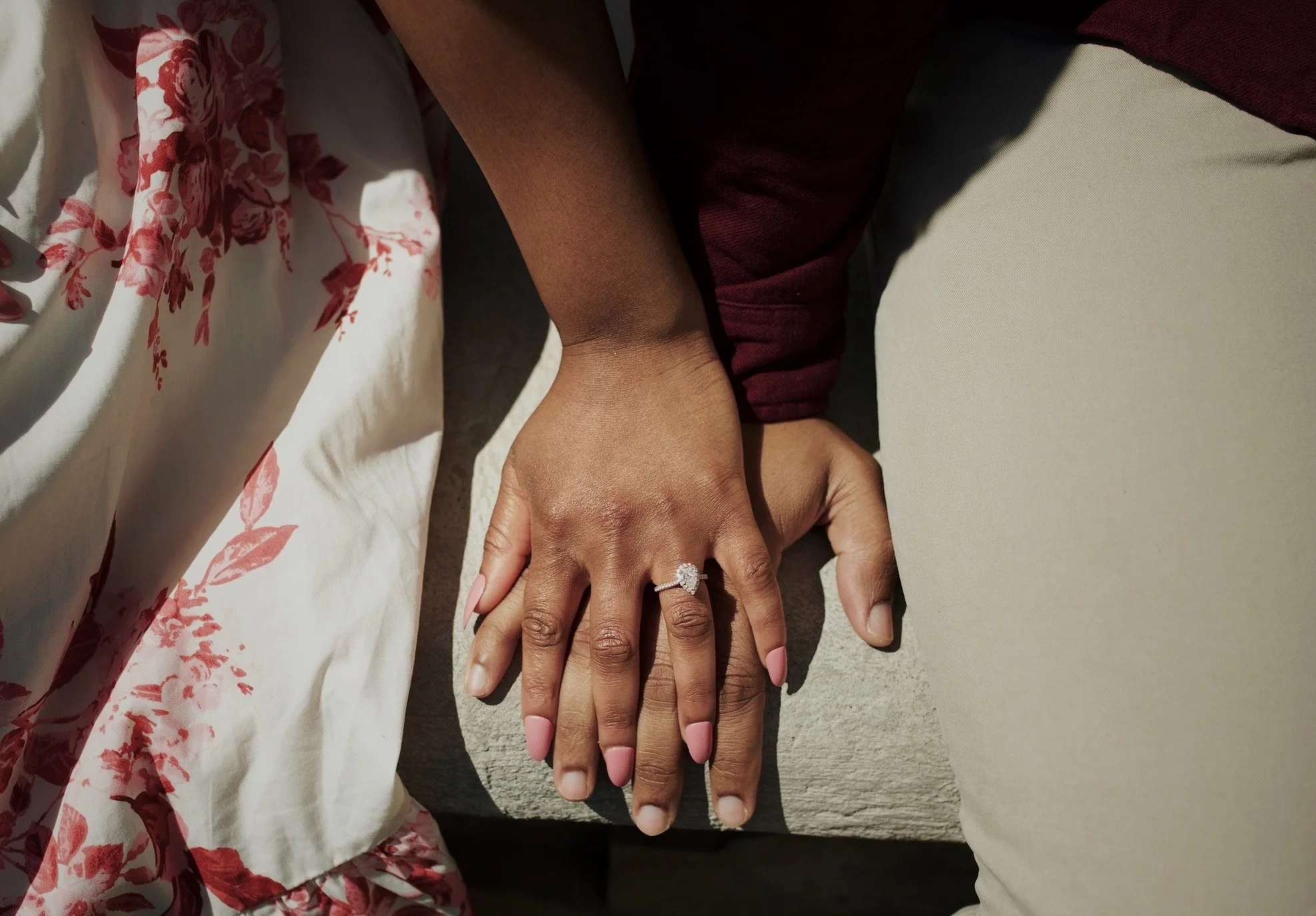 Close-up of a couple holding hands, with a diamond engagement ring on the woman's finger, sitting outside.