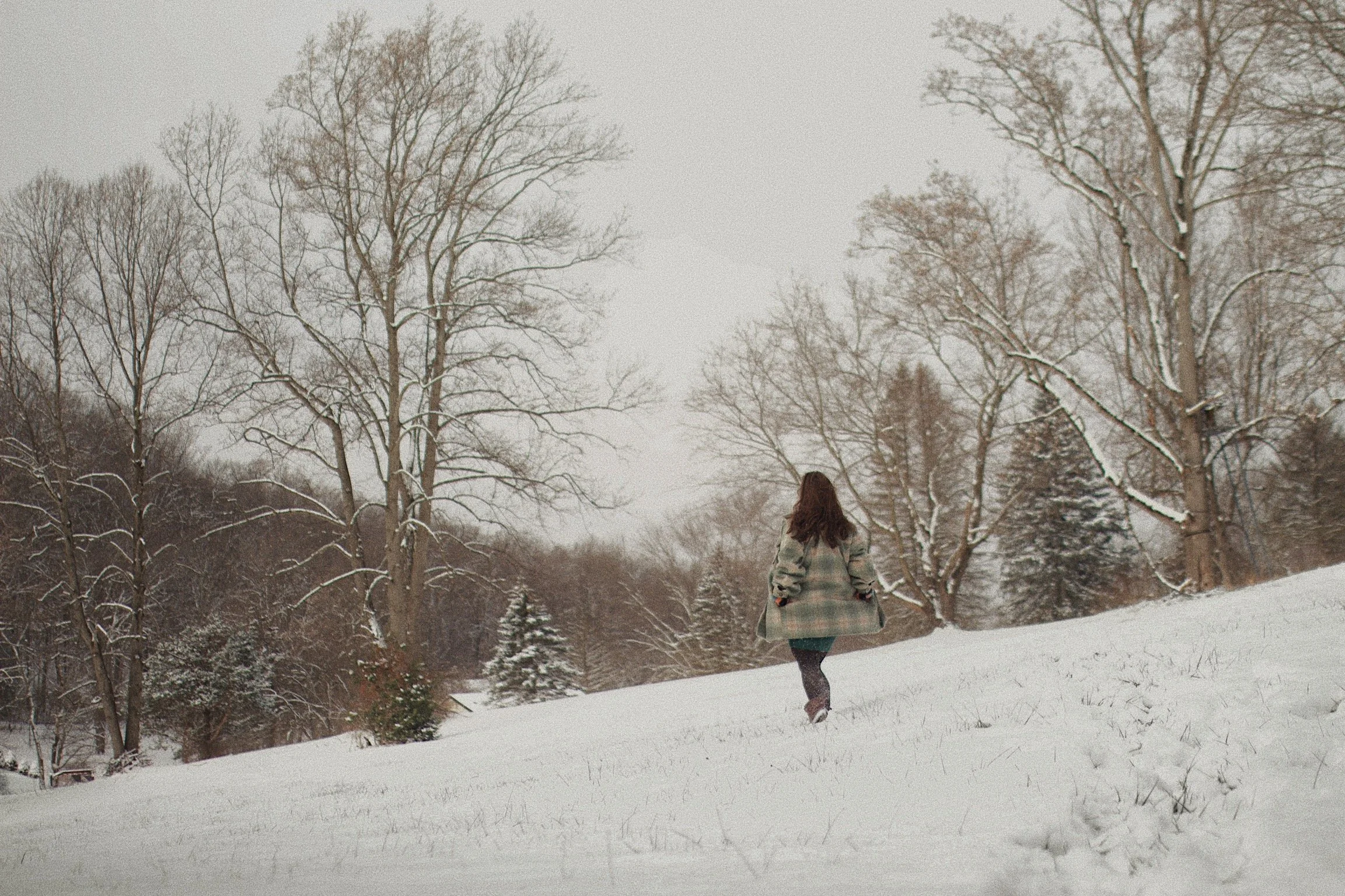 Woman walking through a snow-covered park with trees during winter.