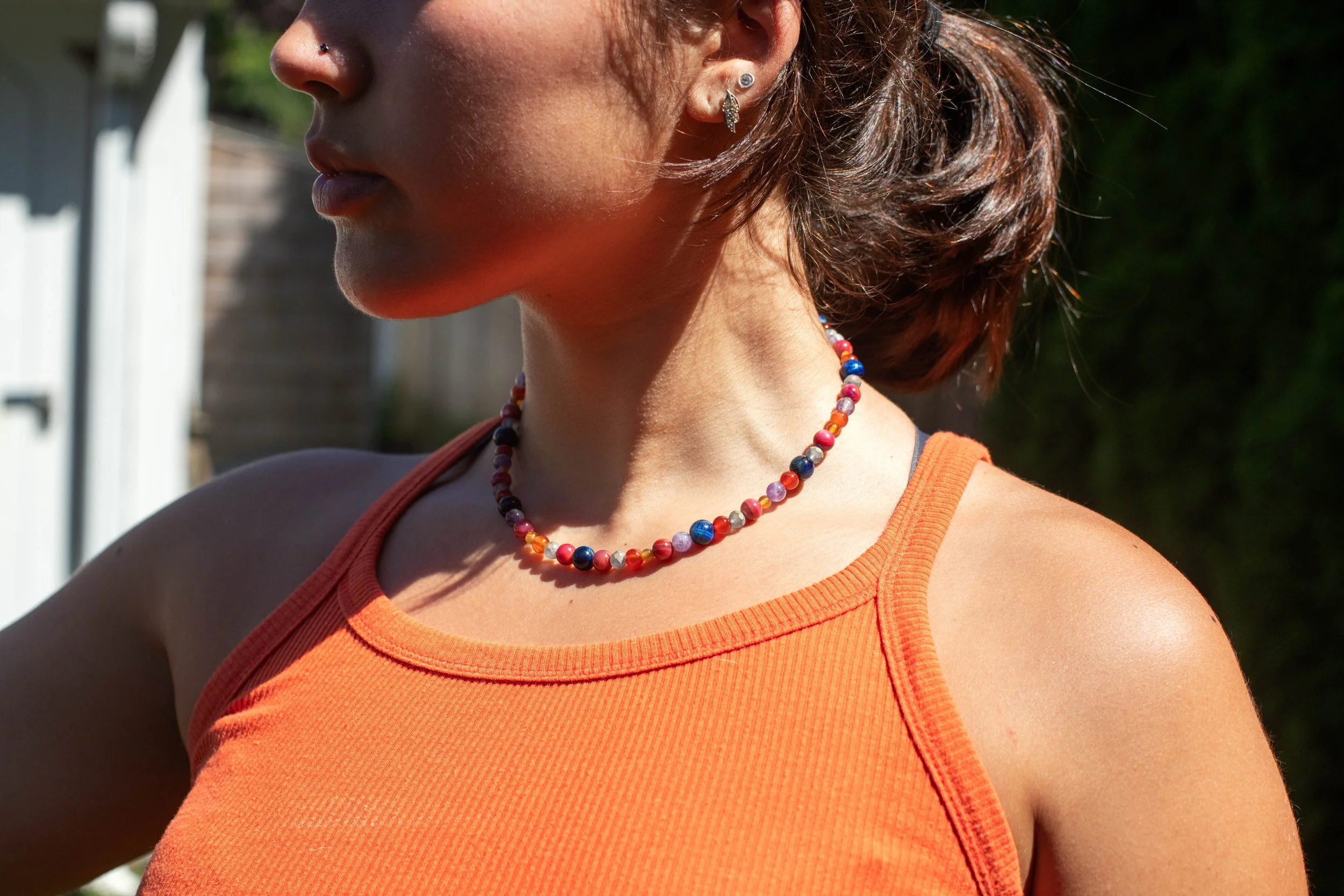 Person wearing an orange tank top and a colorful bead necklace, outdoors.