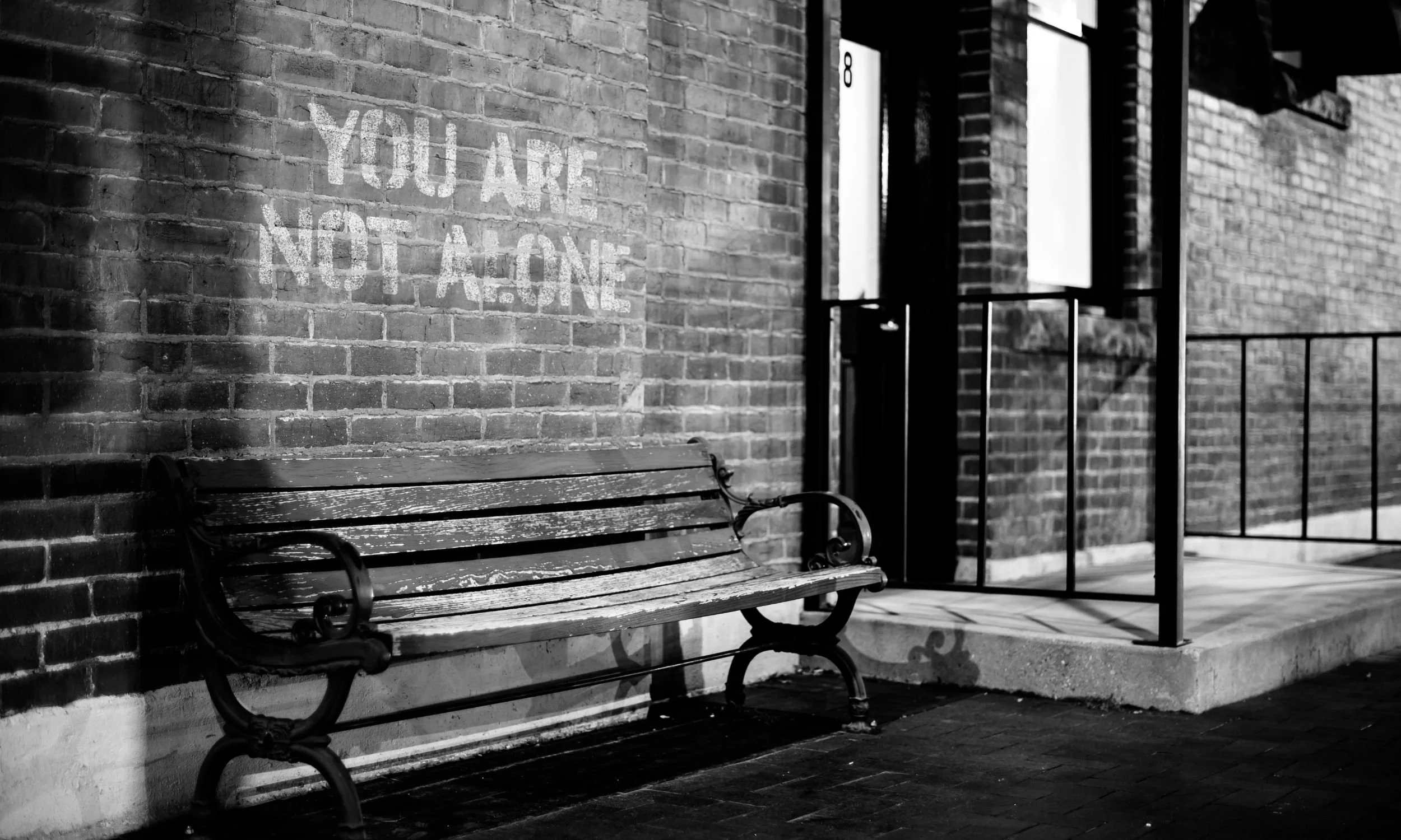 Bekkur við múr þar sem textinn you are not alone sést á vegg, vísun í stuðning og samstöðu.