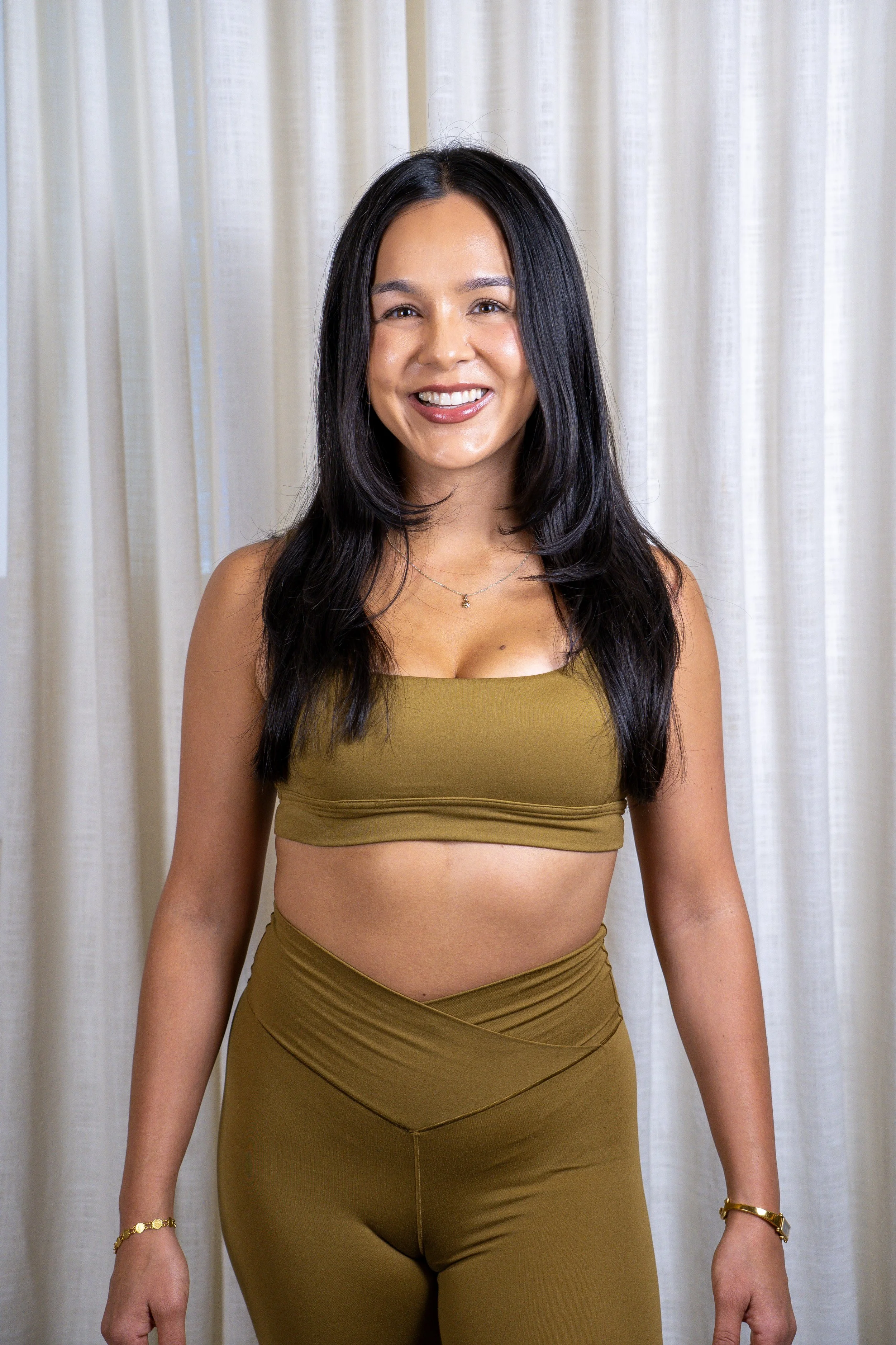 A woman with long dark hair smiling, wearing a light blue romper and a blue patterned cover-up, standing against a plain background.