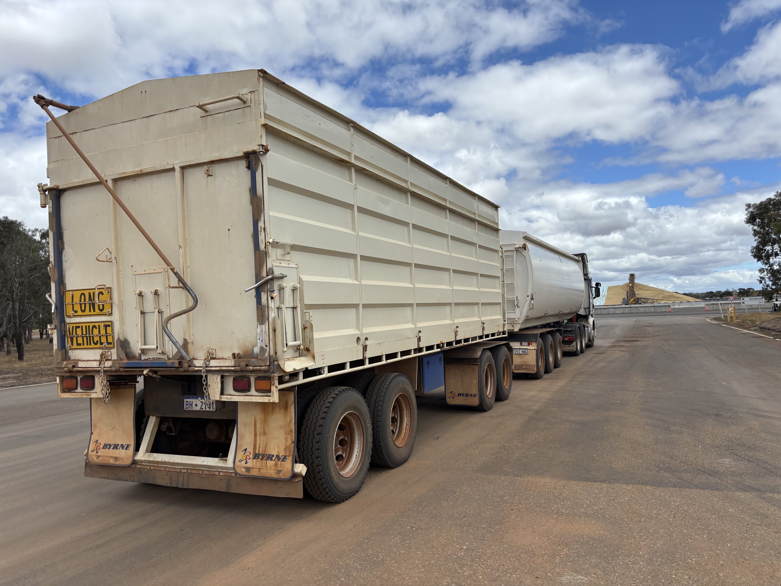 A long semi-trailer truck parked on a rural road, under a partly cloudy sky, with a sign indicating 'Long Vehicle' on the rear.