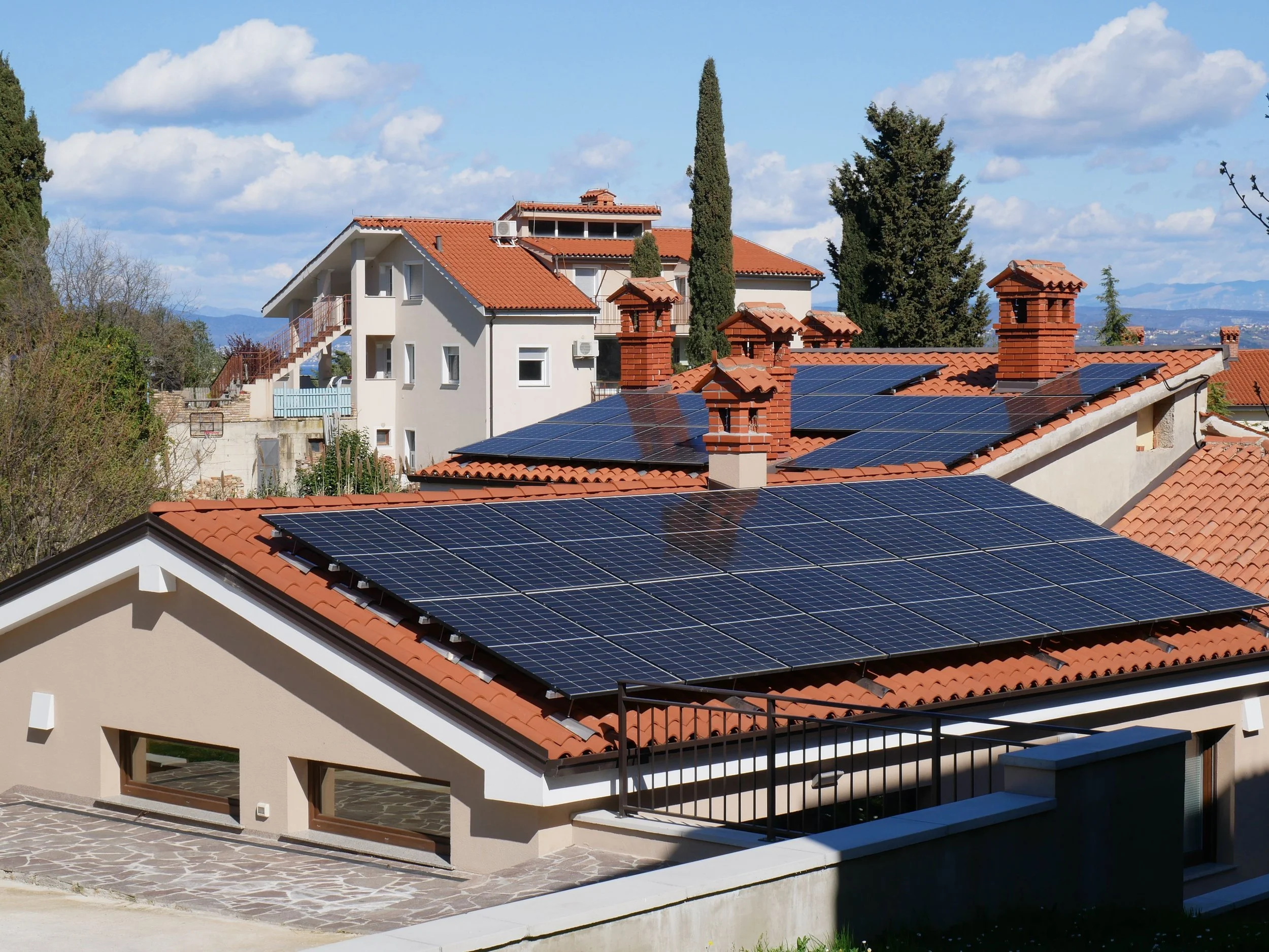 Panoramic view of suburban homes with red tile rooftops fitted with solar panels under a bright sunny sky, illustrating peak sun hours and residential solar energy generation.