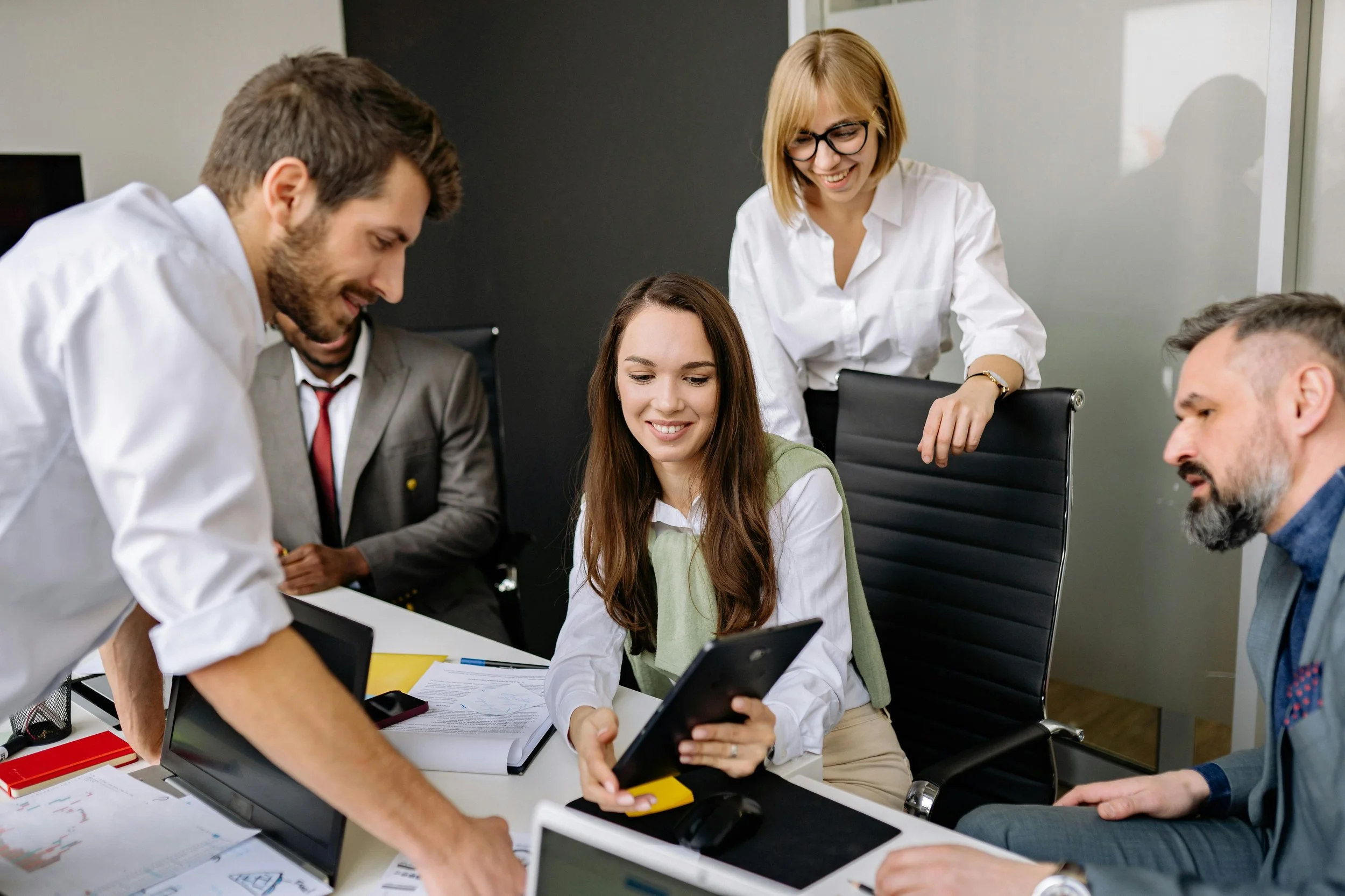A woman sitting at a desk with colleagues, showing a tablet during a discussion about measuring and reducing carbon footprints.
