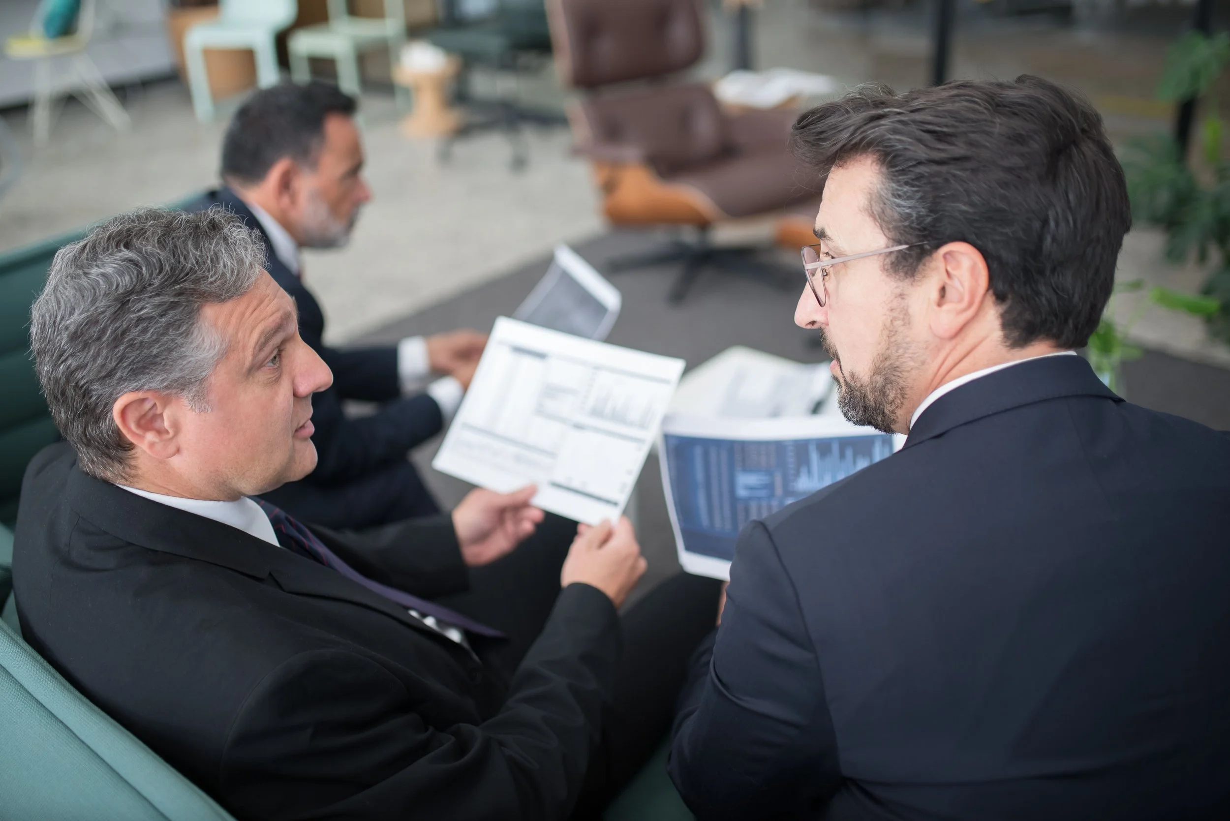 Three businessmen discussing documents together in a modern office, representing effective workplace communication, professional collaboration, and leadership relationships.