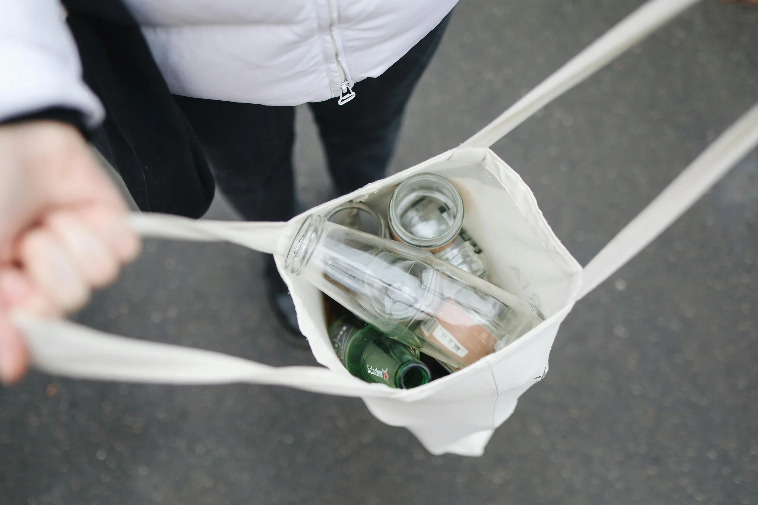 Man opening a reusable tote bag filled with glass bottles, representing sustainable living and waste reduction practices.