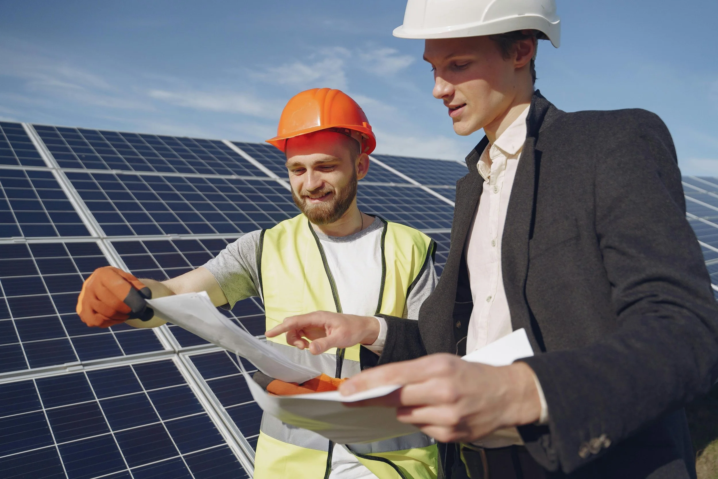 Two solar energy experts reviewing technical documents while standing beside installed solar panels, discussing system design and performance.
