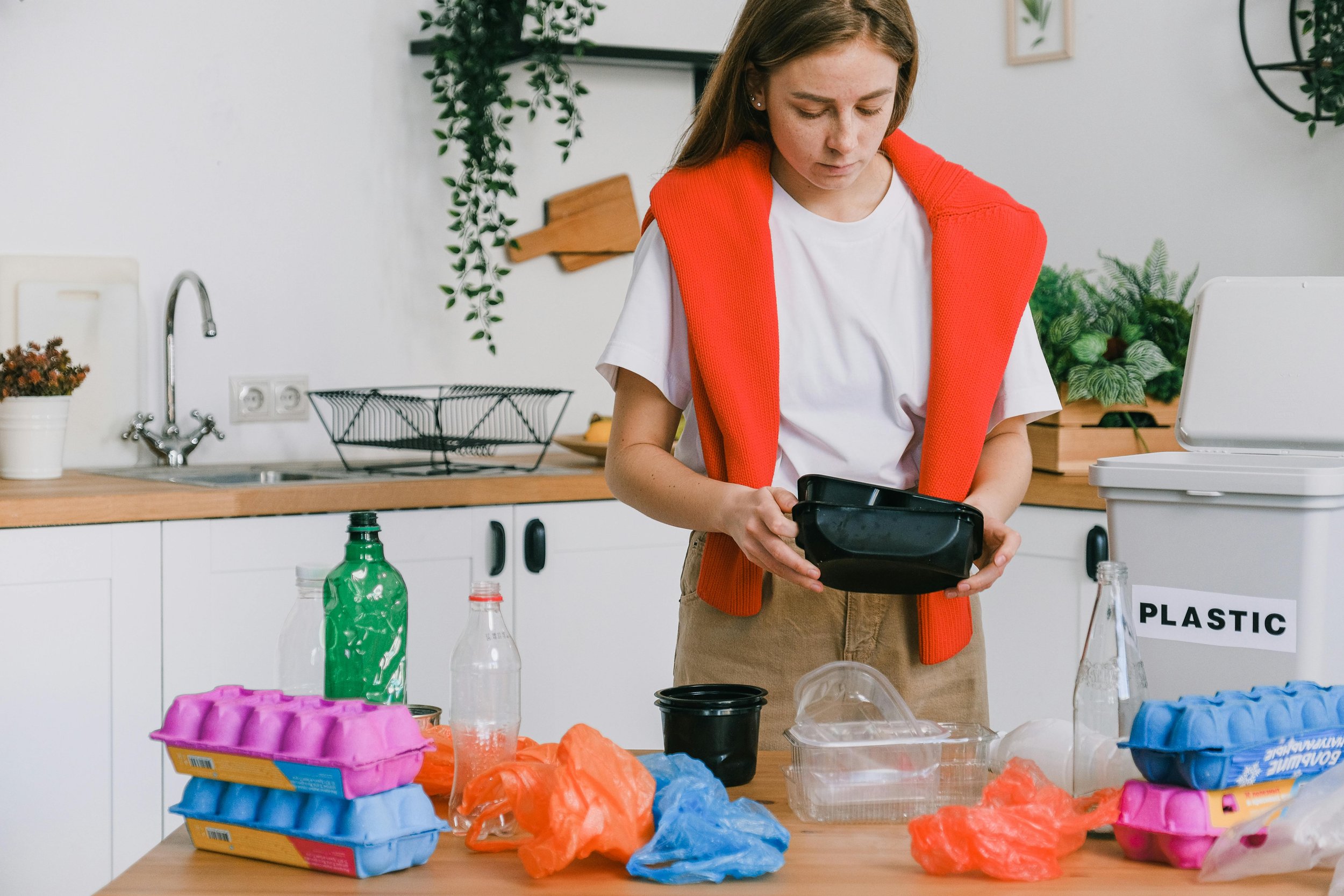 Flat lay of everyday household items like cleaning bottles, clothing, and plastic packaging contrasted with eco-friendly alternatives such as bamboo brushes and reusable containers.