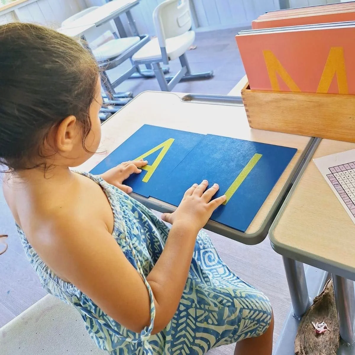 Enfant manipulant des lettres rugueuses majuscules dans une activité Montessori à l’École Fare Anuanua à Moorea