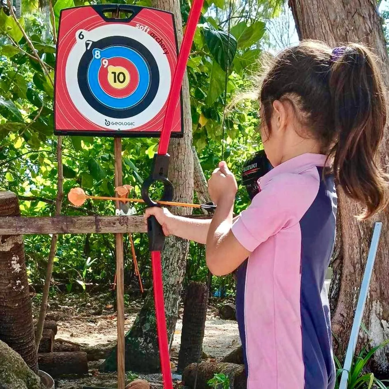 Enfant participant à un atelier de tir à l’arc lors d’une sortie éducative sur le motu pendant les stages vacances à l’École Fare Anuanua
