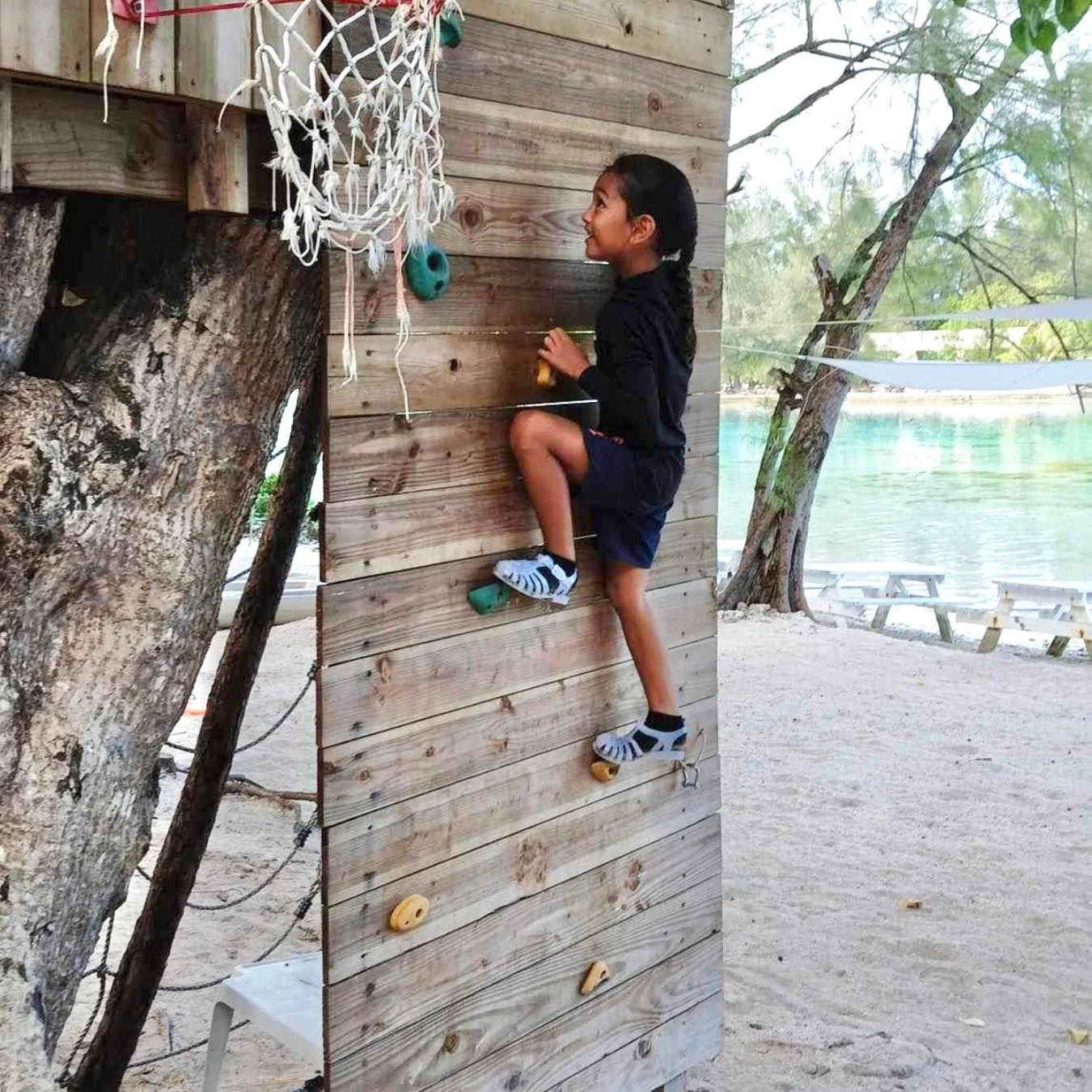 Enfant escaladant une structure de jeu lors d’une sortie au motu pendant les stages vacances de l’École Fare Anuanua à Moorea