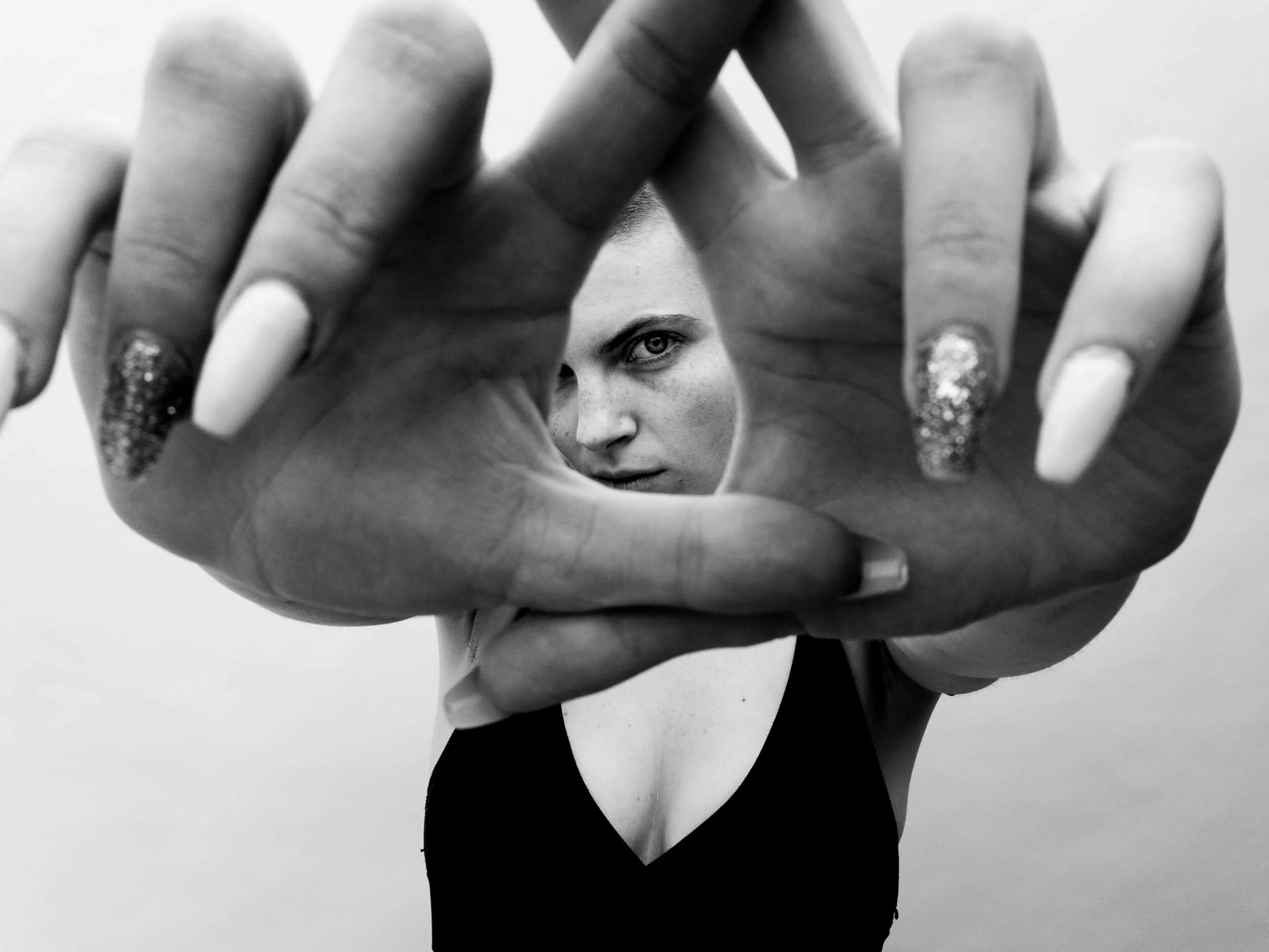 Parker J Pfister Black and White Fine Art Portrait of a white woman holder her hands up at the camera while looking through them.