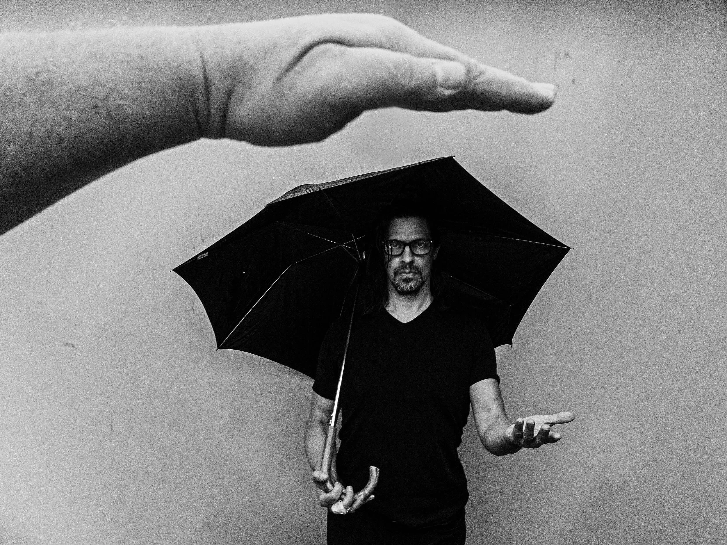 Parker J Pfister Fine Art Photography with a hand in the foreground over a man holding an umbrella in the background.