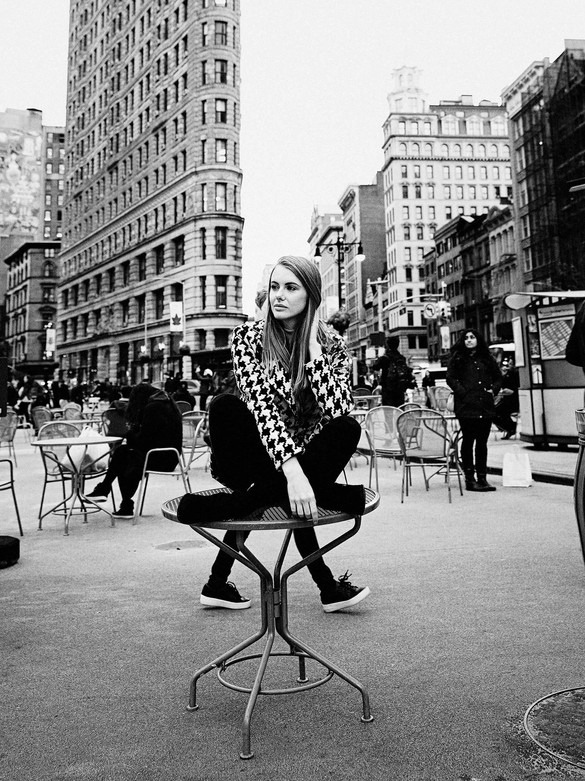 Parker J Pfister Fine Art Black and White Photography of a white woman sitting on a tall chair on a busy street corner.