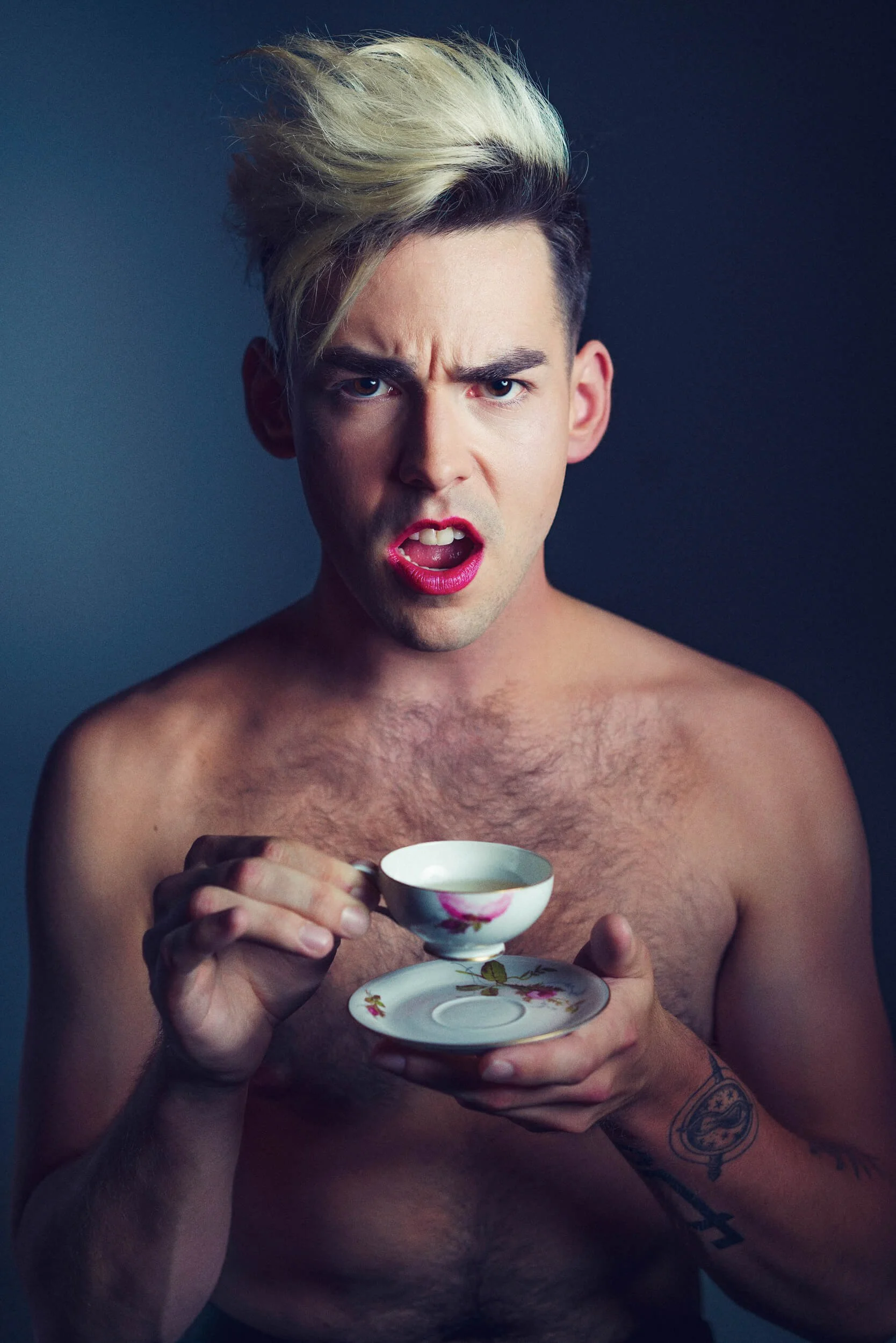 Parker J Pfister Fine Art Portrait of a white man with bleached hair, no shirt, and red lips holding a tea cup looking at the camera.