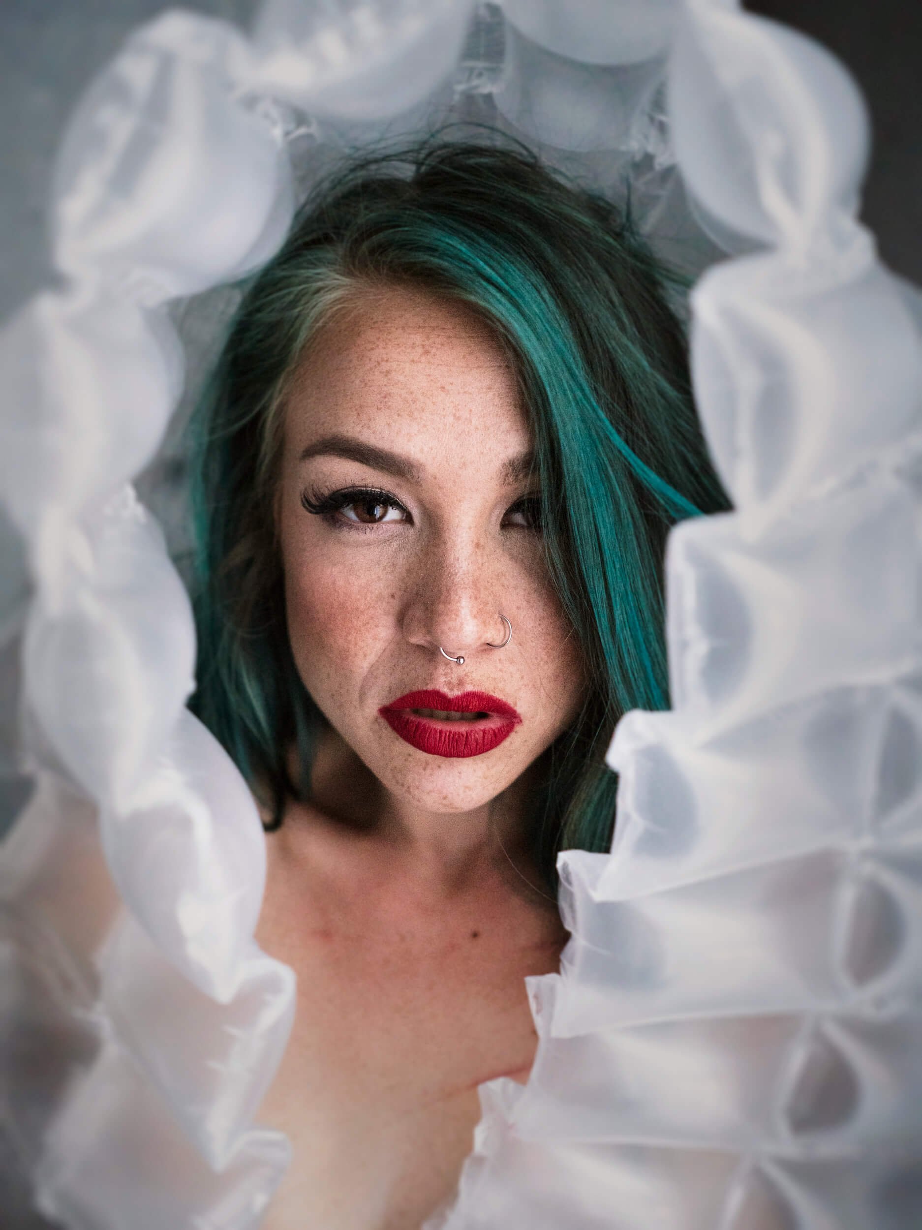 Parker J Pfister Fine Art Portrait of a white woman with green highlighted hair looking at the camera through plastic packing material. 