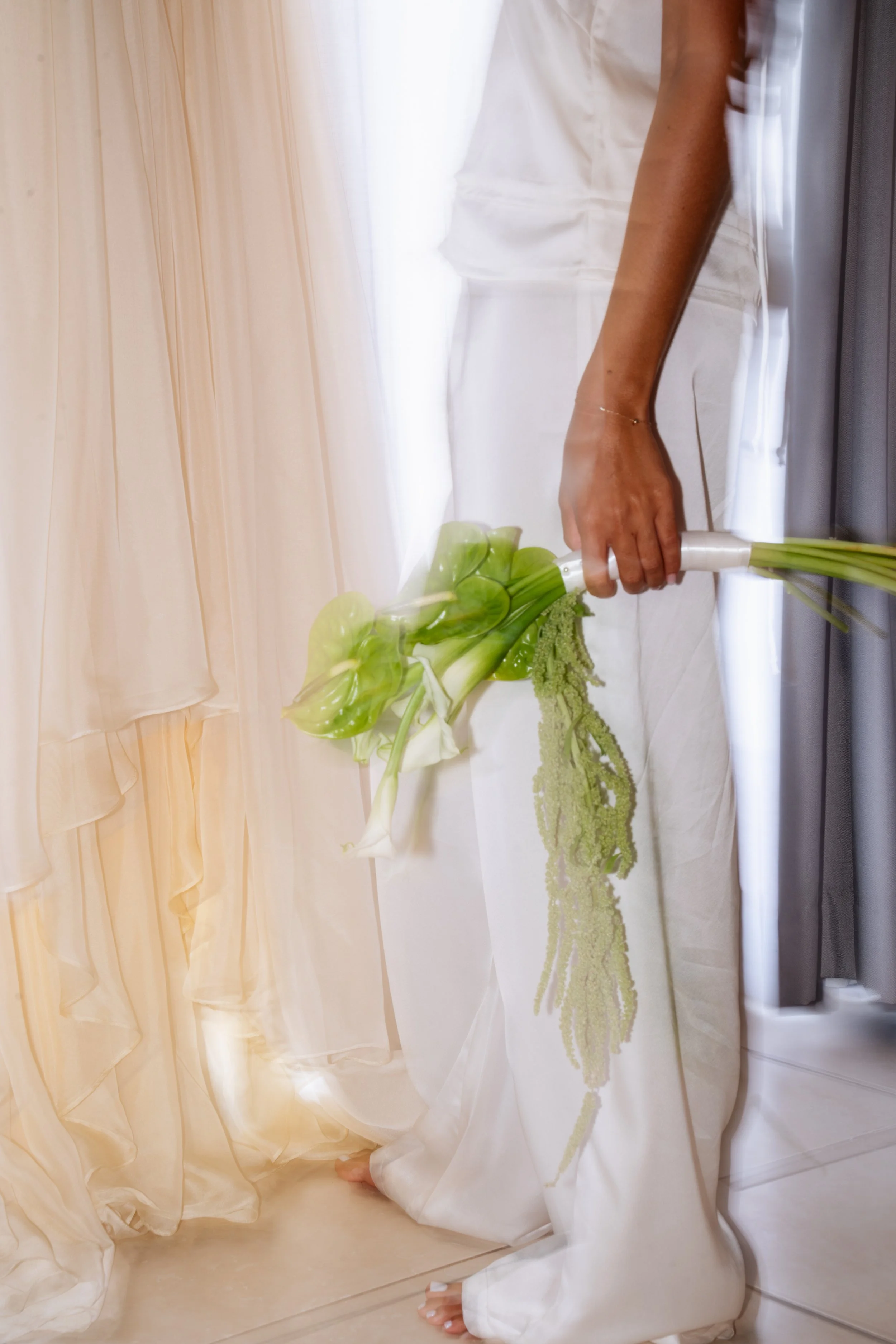 Person in white attire holding a bouquet of white and green flowers near a window.